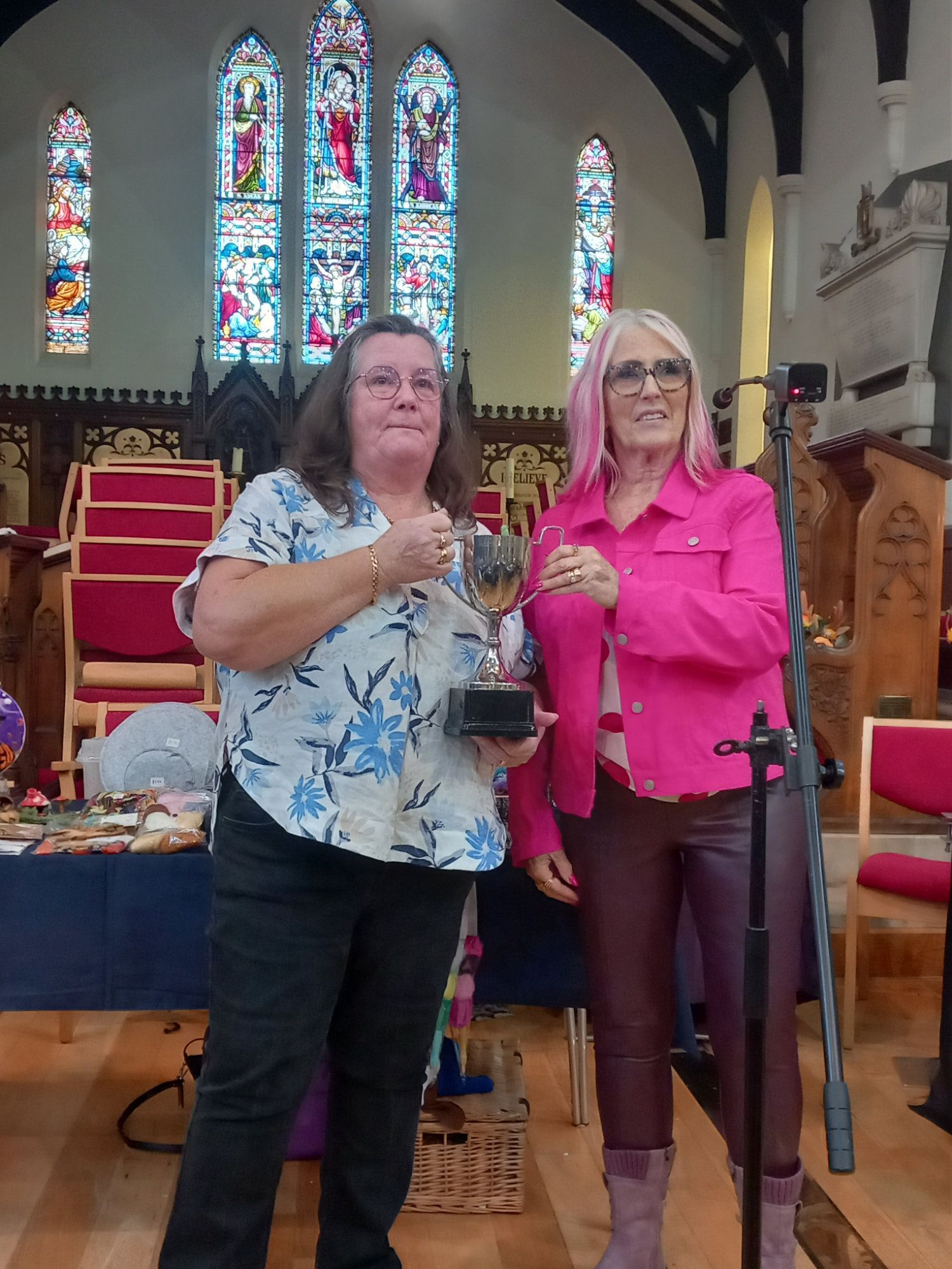 Two women are standing next to each other in a church holding a trophy.