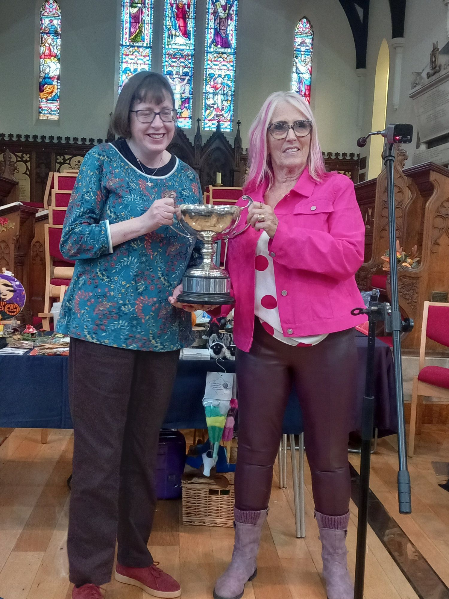 Two women are standing next to each other in a church holding a trophy.