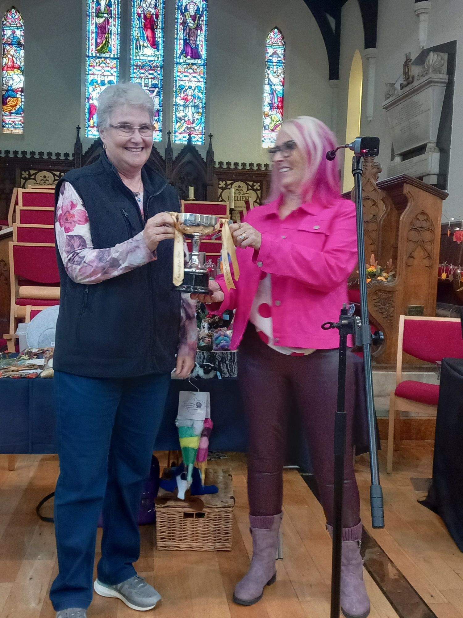 Two women are standing next to each other in front of a microphone in a church.