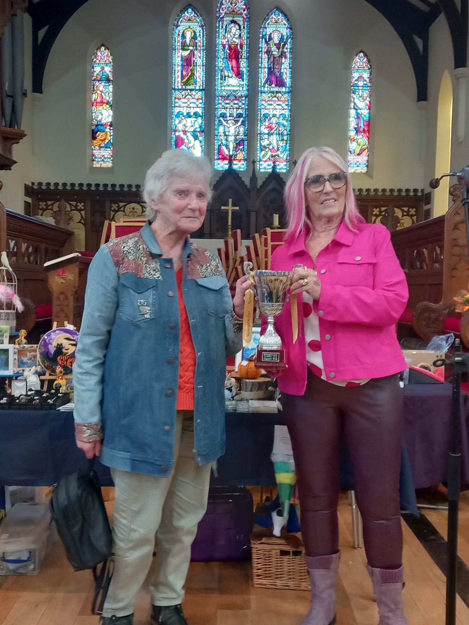 Two women are standing in front of a stained glass window in a church.