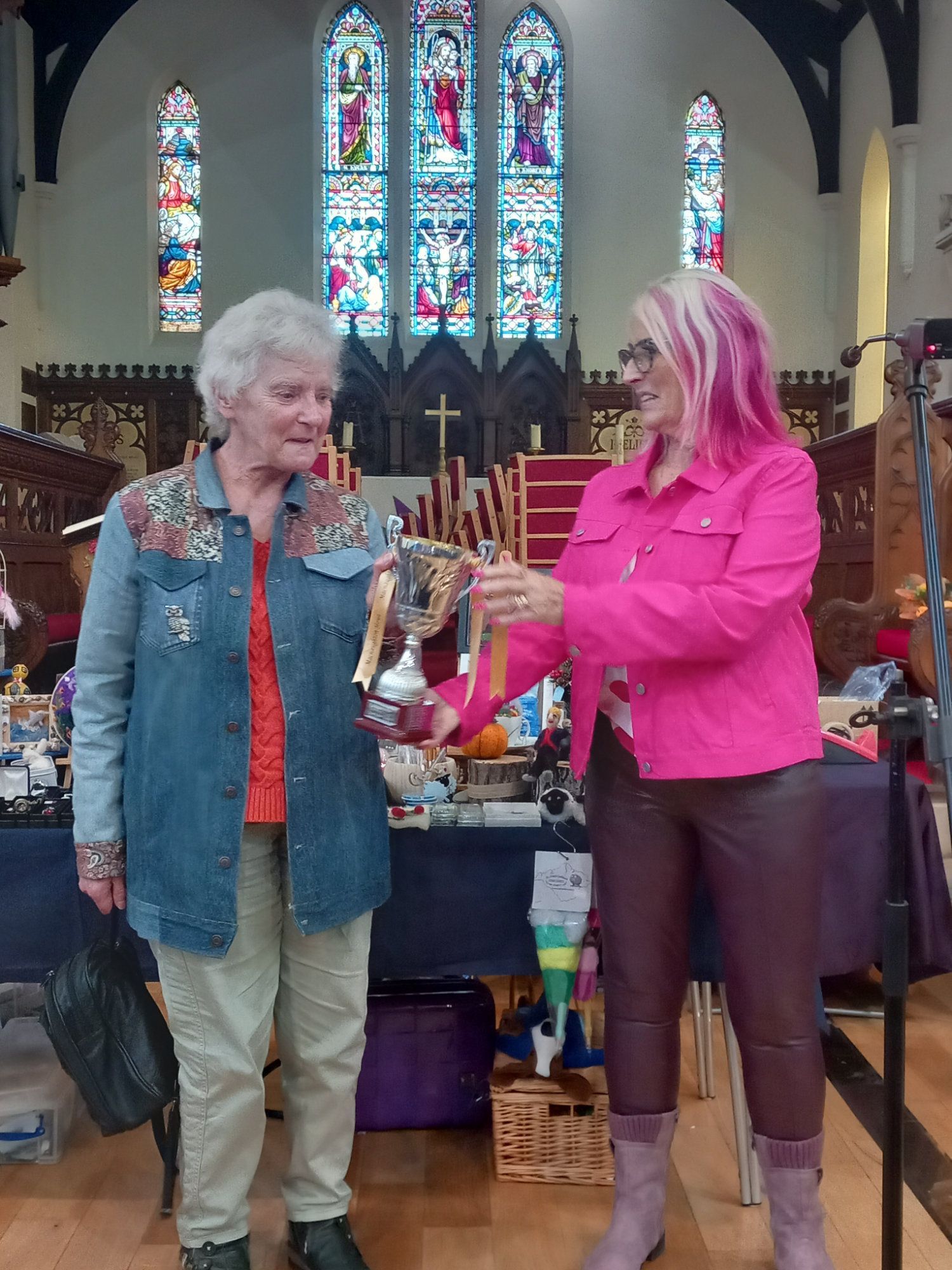 Two women are standing next to each other in a church holding a trophy.