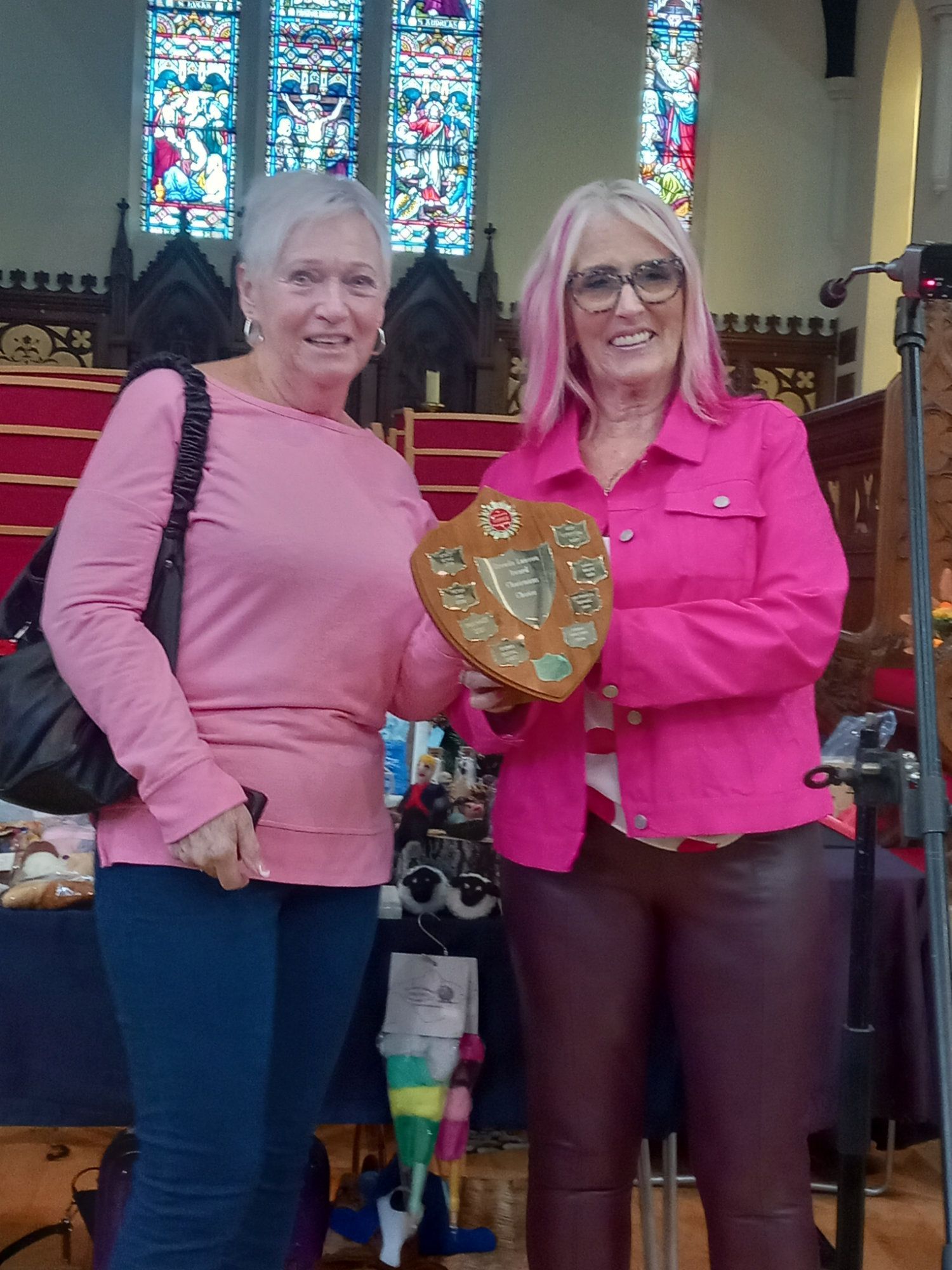 Two women are standing next to each other holding a plaque in front of a stained glass window.