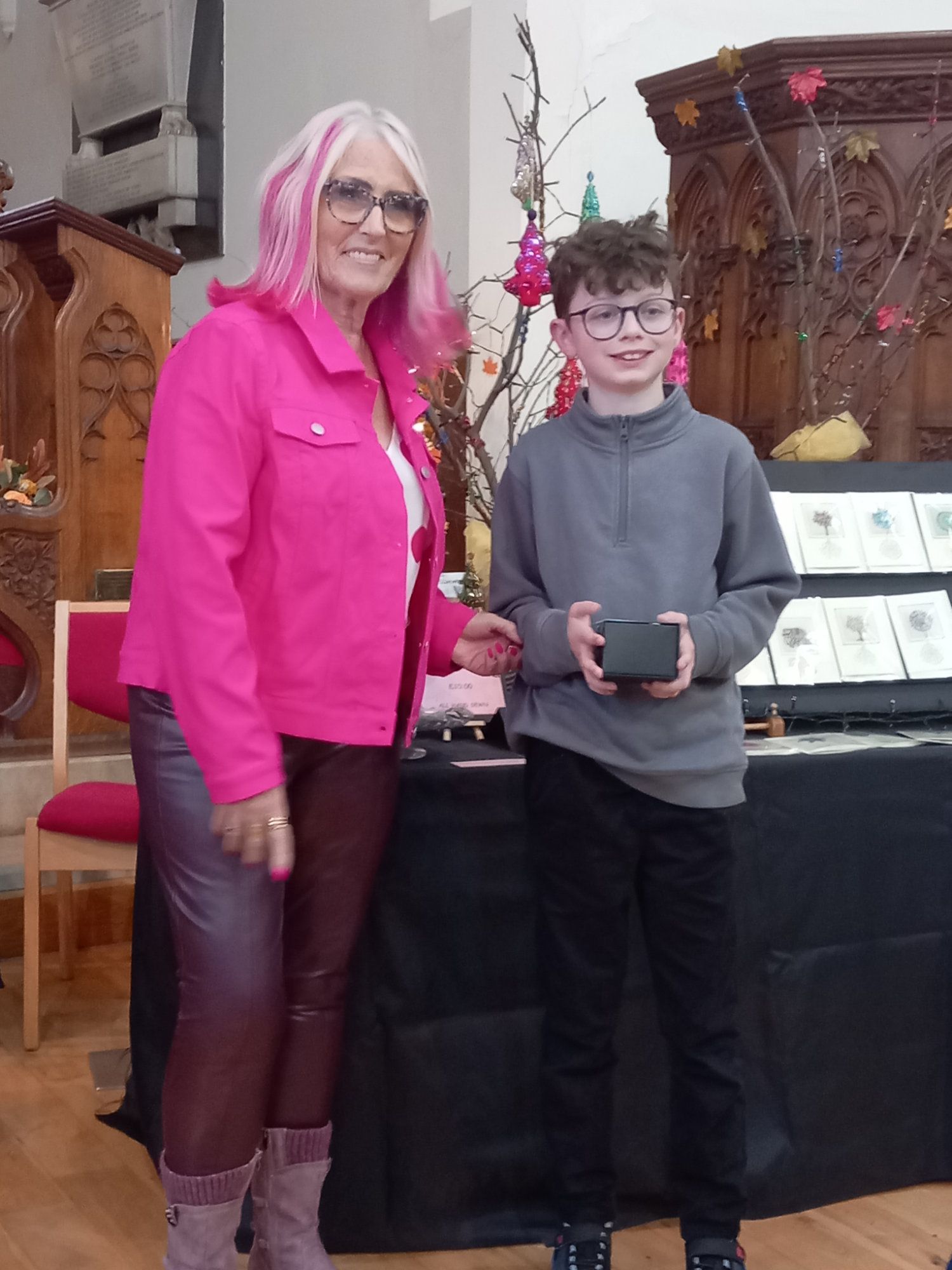 A woman in a pink jacket is standing next to a boy in a gray shirt.