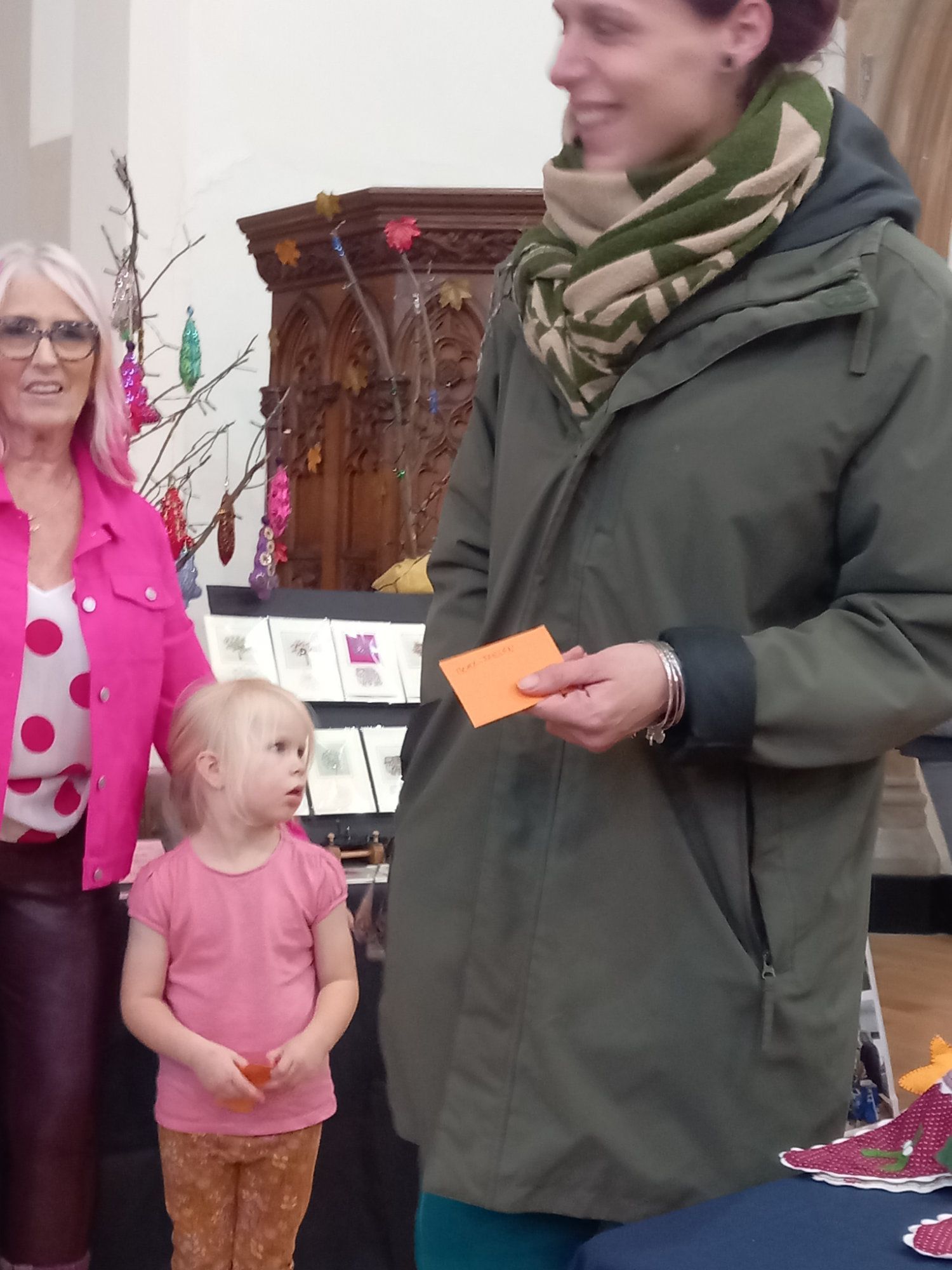 A woman in a green jacket stands next to a little girl in a pink shirt