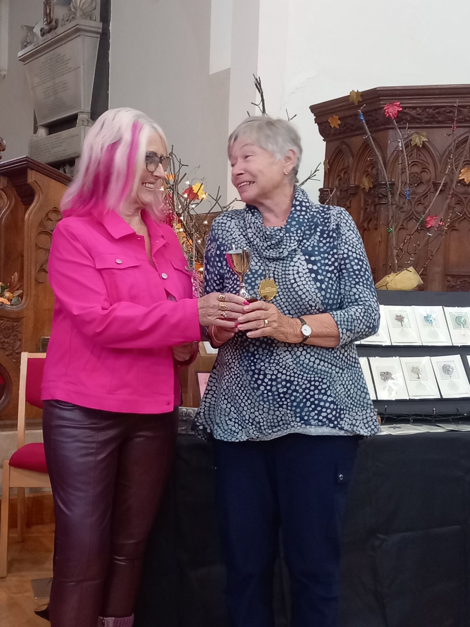 Two women are standing next to each other in a room holding wine glasses.