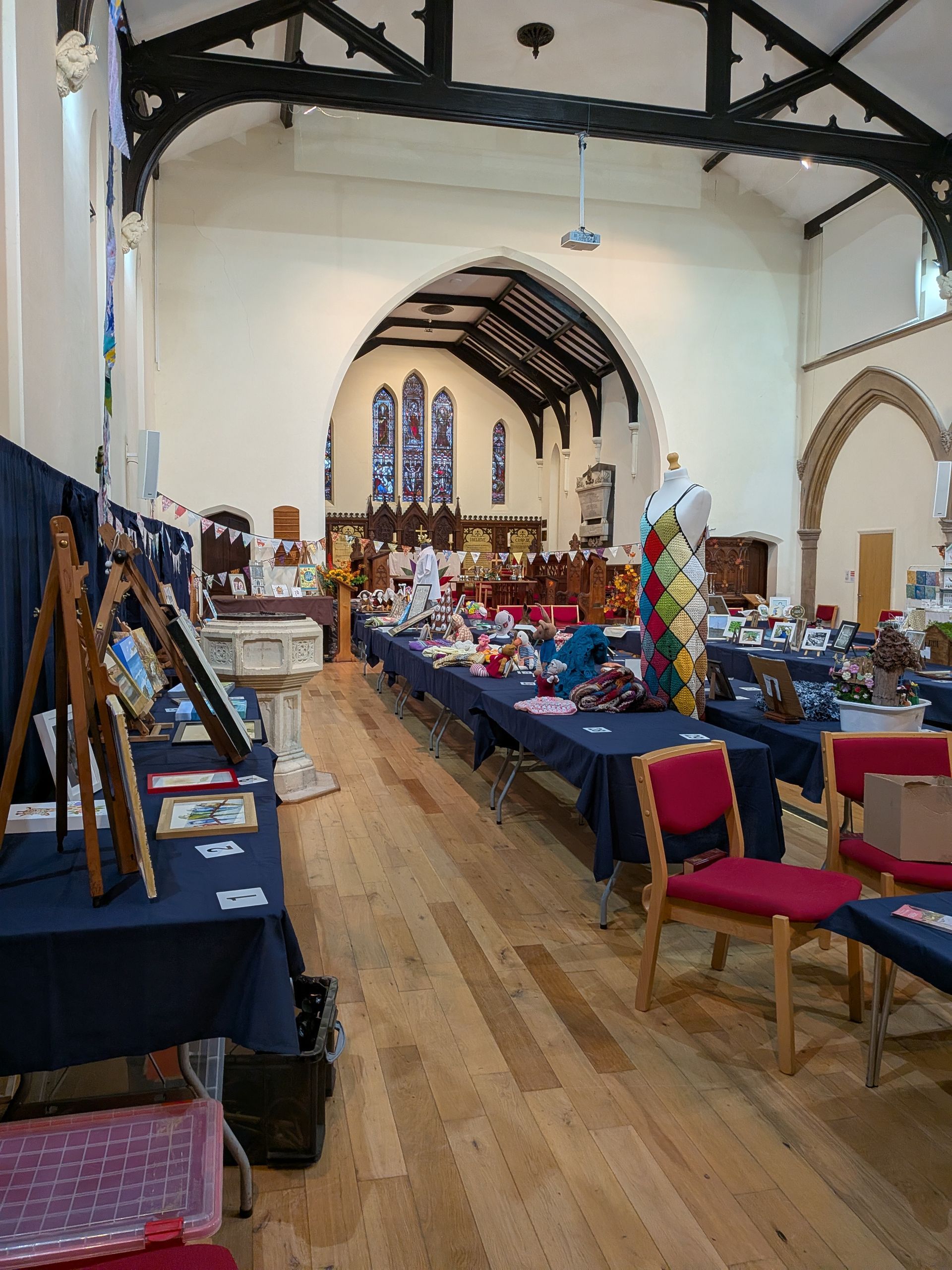 Tables with items for sale in a church hall, a mannequin, stained glass windows.