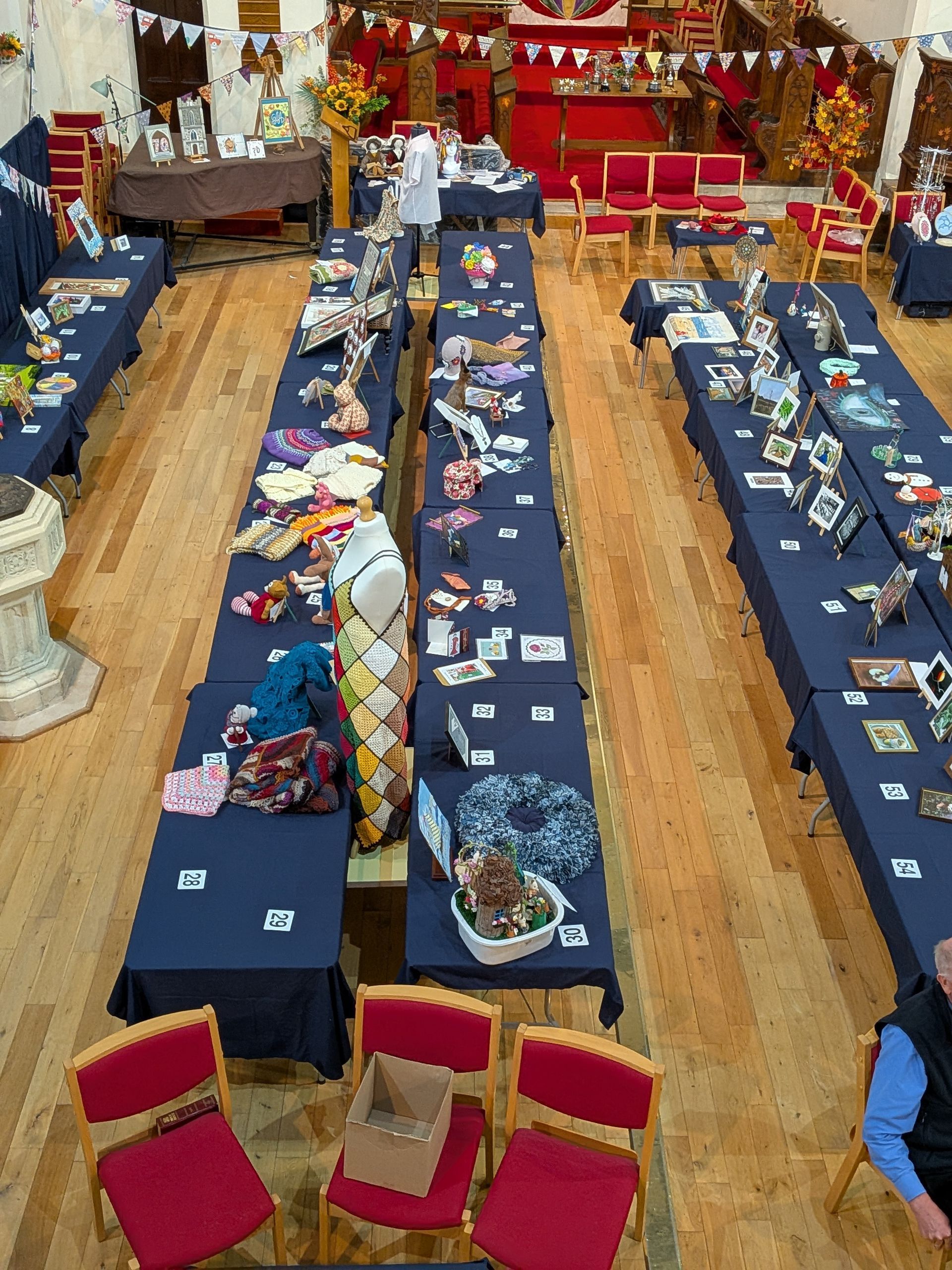 A craft fair in a hall with long tables covered in blue cloths displaying handmade items.