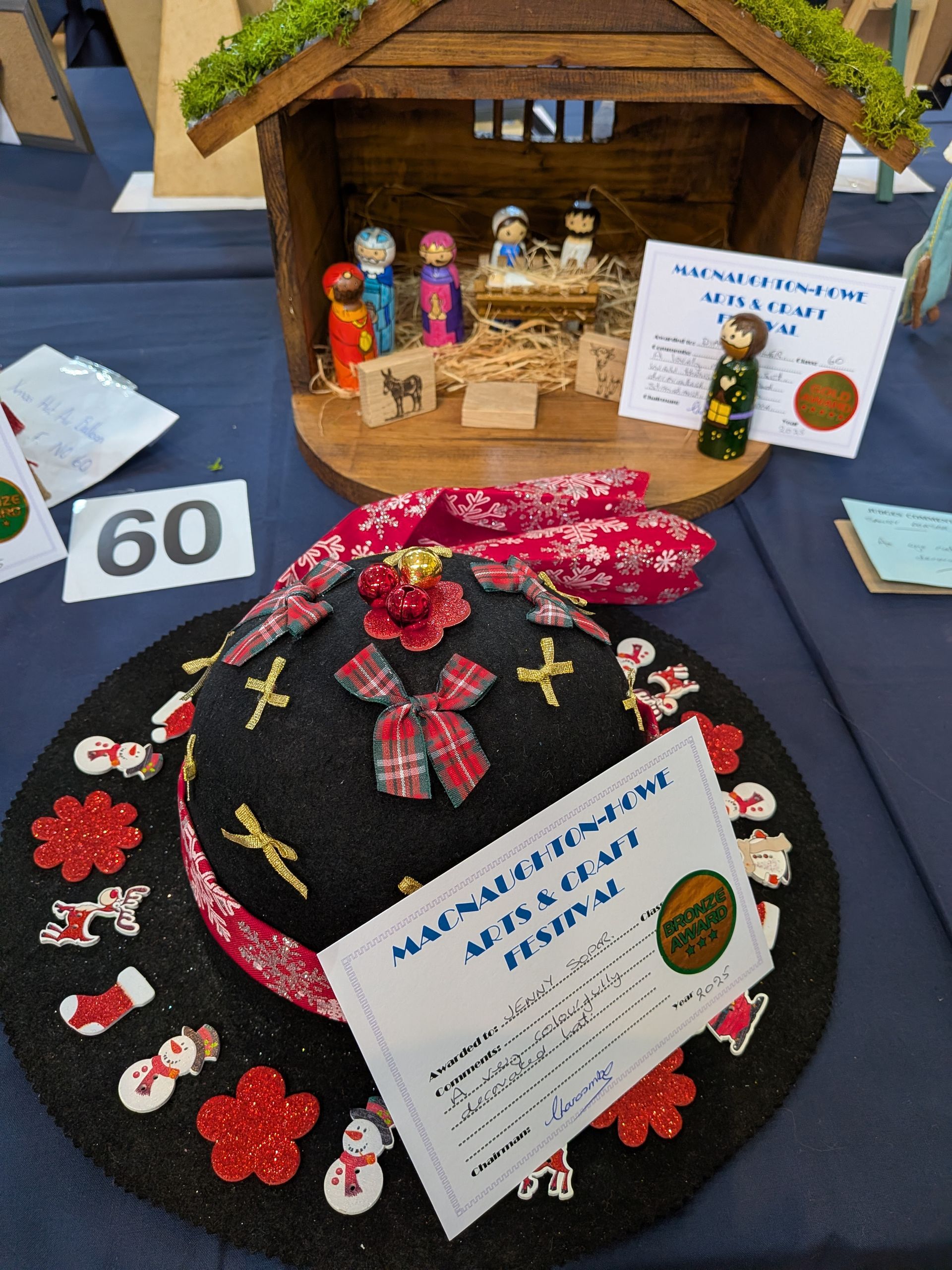 Nativity scene and decorated hat on a table at an art festival; number 60 sign present.