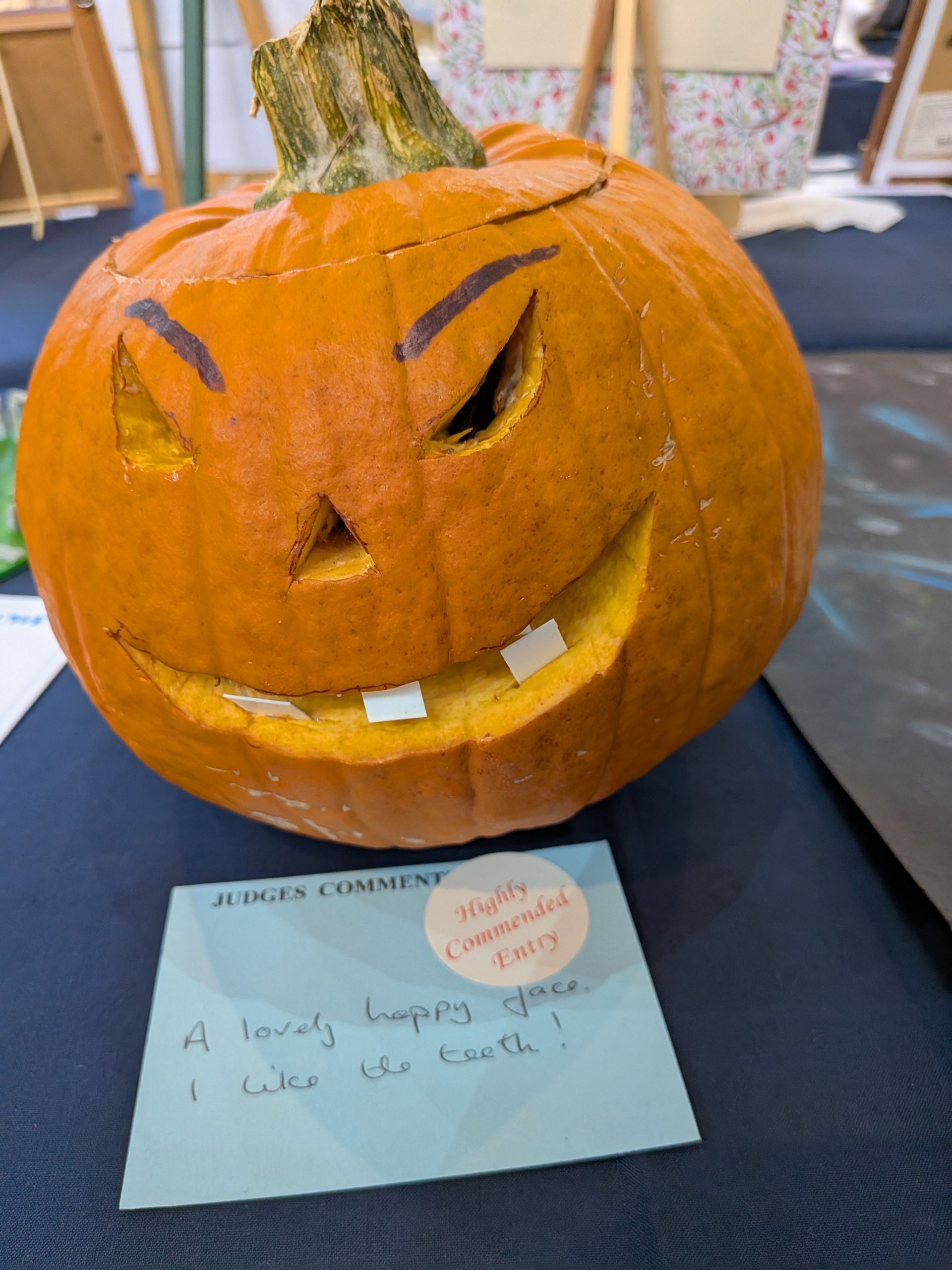 A carved pumpkin with a smiling face and judging comment on a blue table.