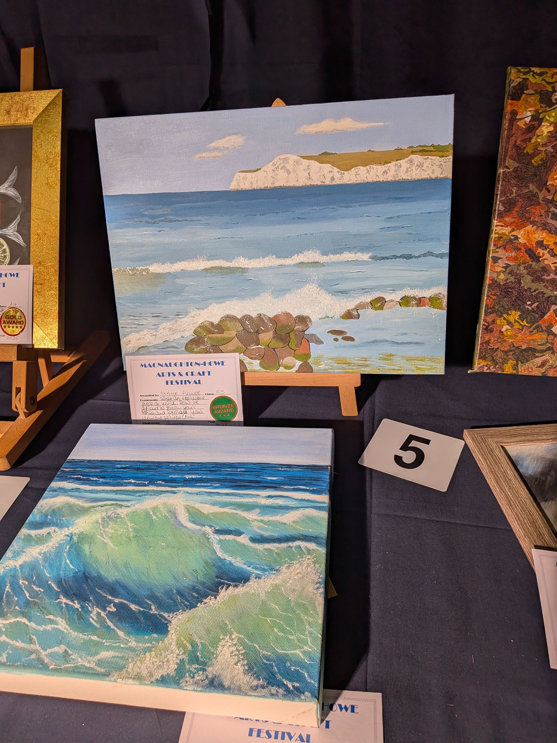 Paintings of ocean waves and a coastal landscape on display.