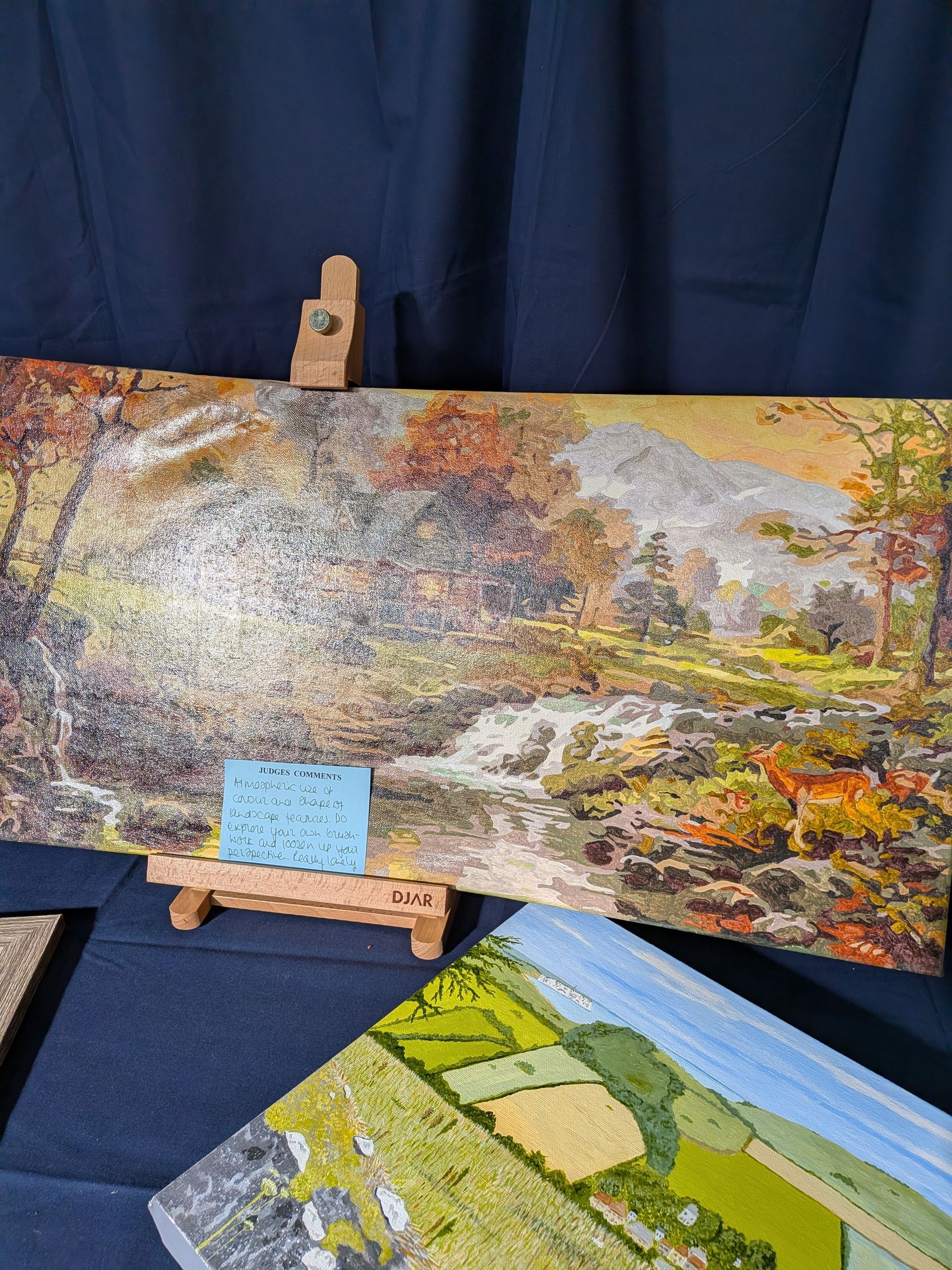 Mosaic art of a stream and forest with fall colors displayed on a small easel.