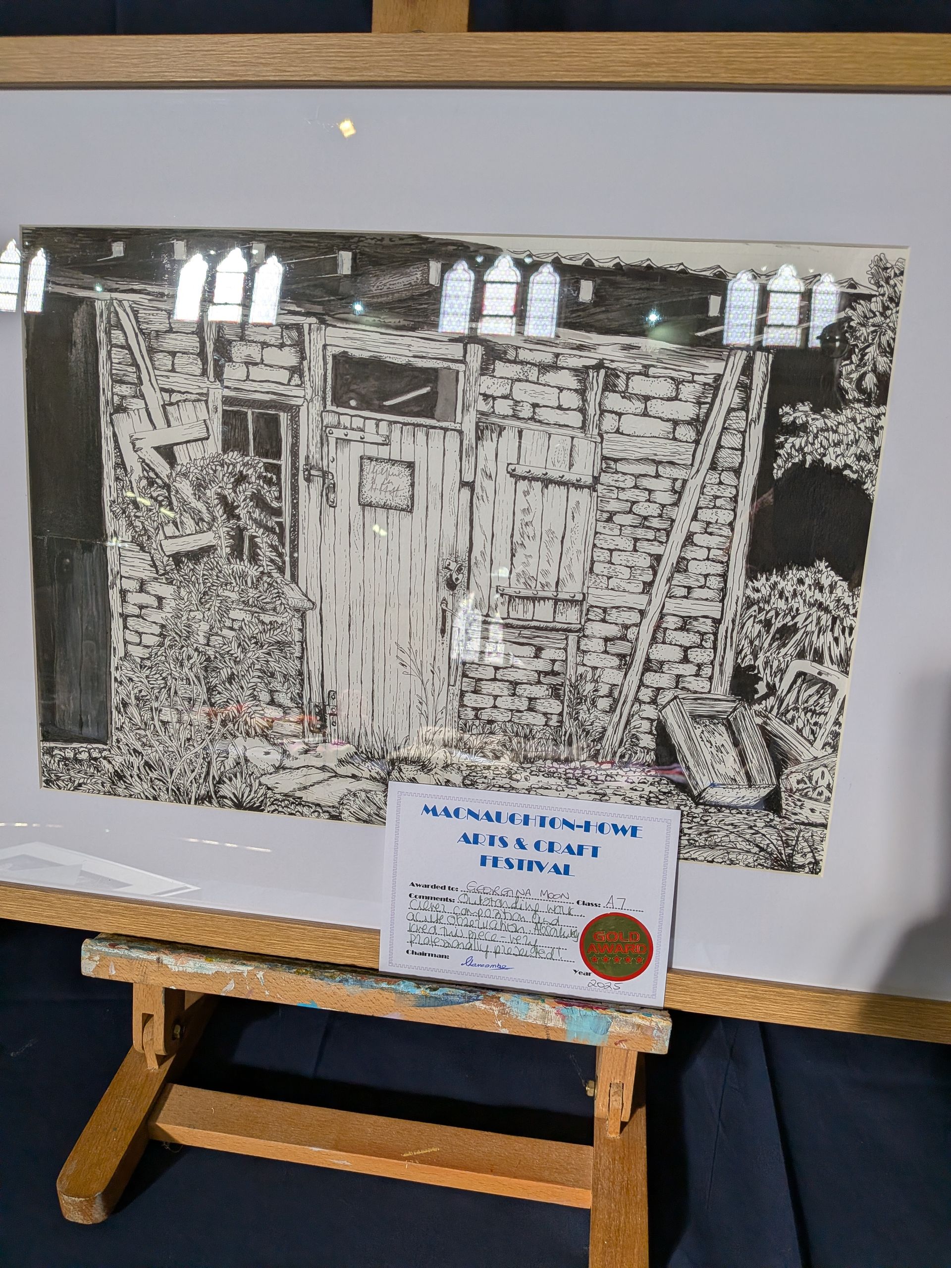 Black and white art print of weathered building with vegetation, displayed on a small wooden easel.