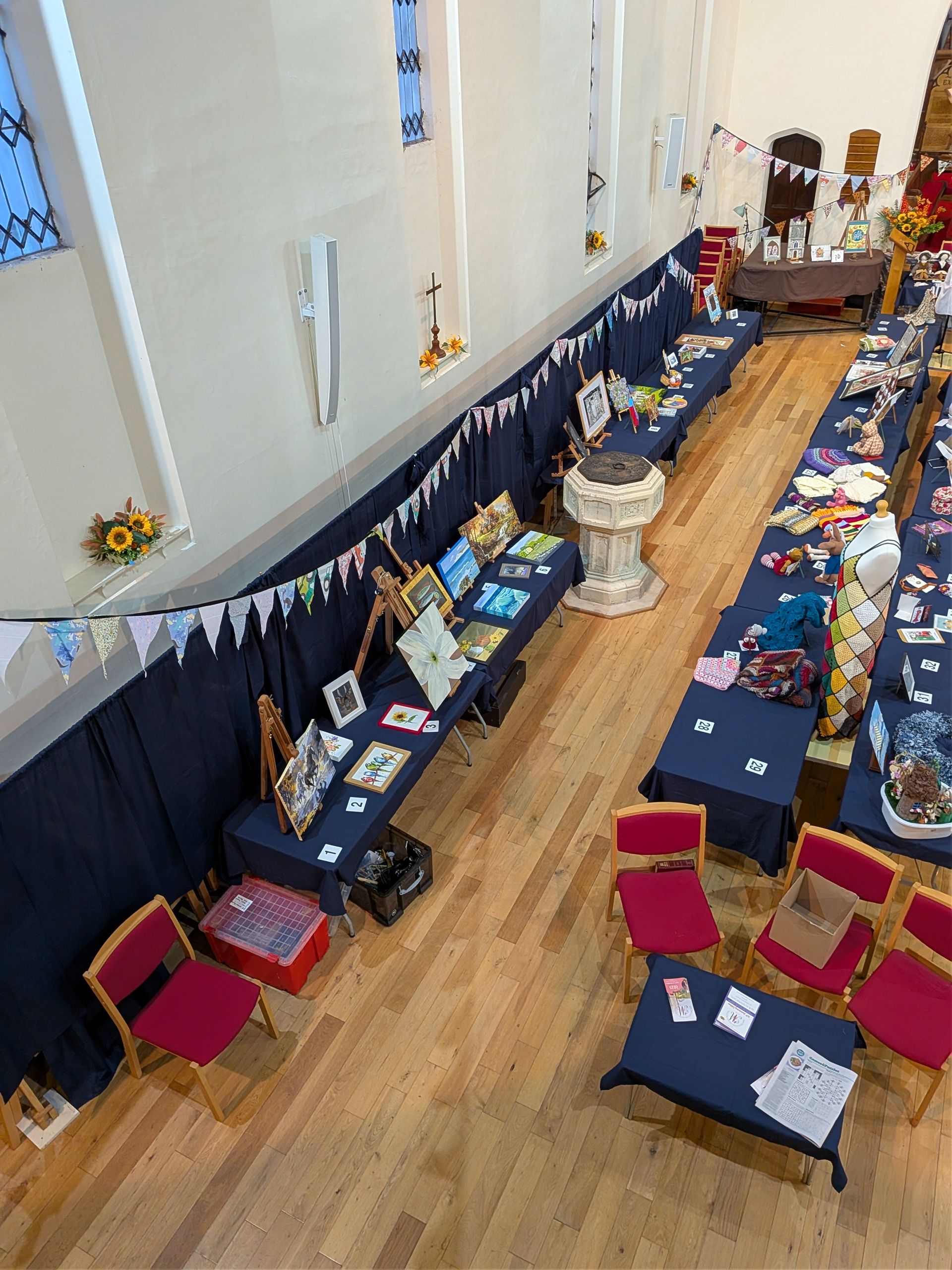 An overhead view of a craft fair in a church hall with vendors displaying goods on tables.