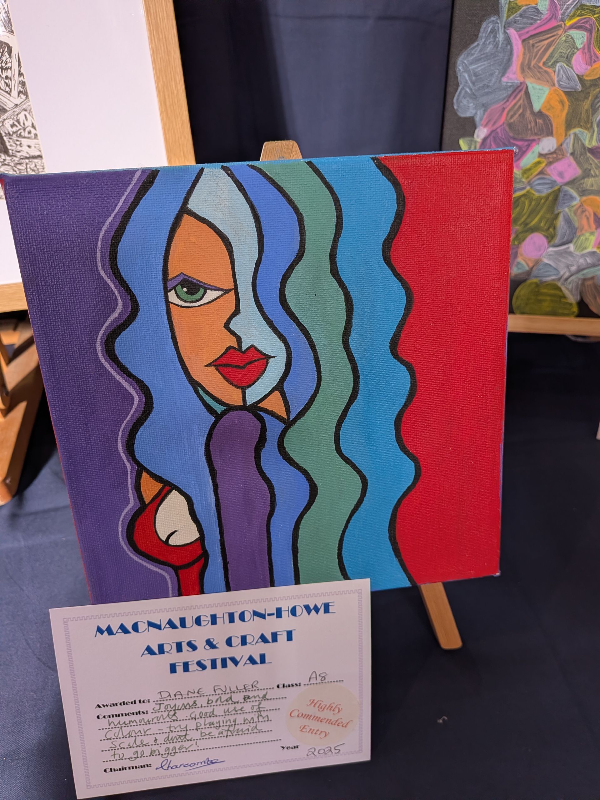 Abstract portrait painting on easel, blue hair, colorful background, art festival sign.
