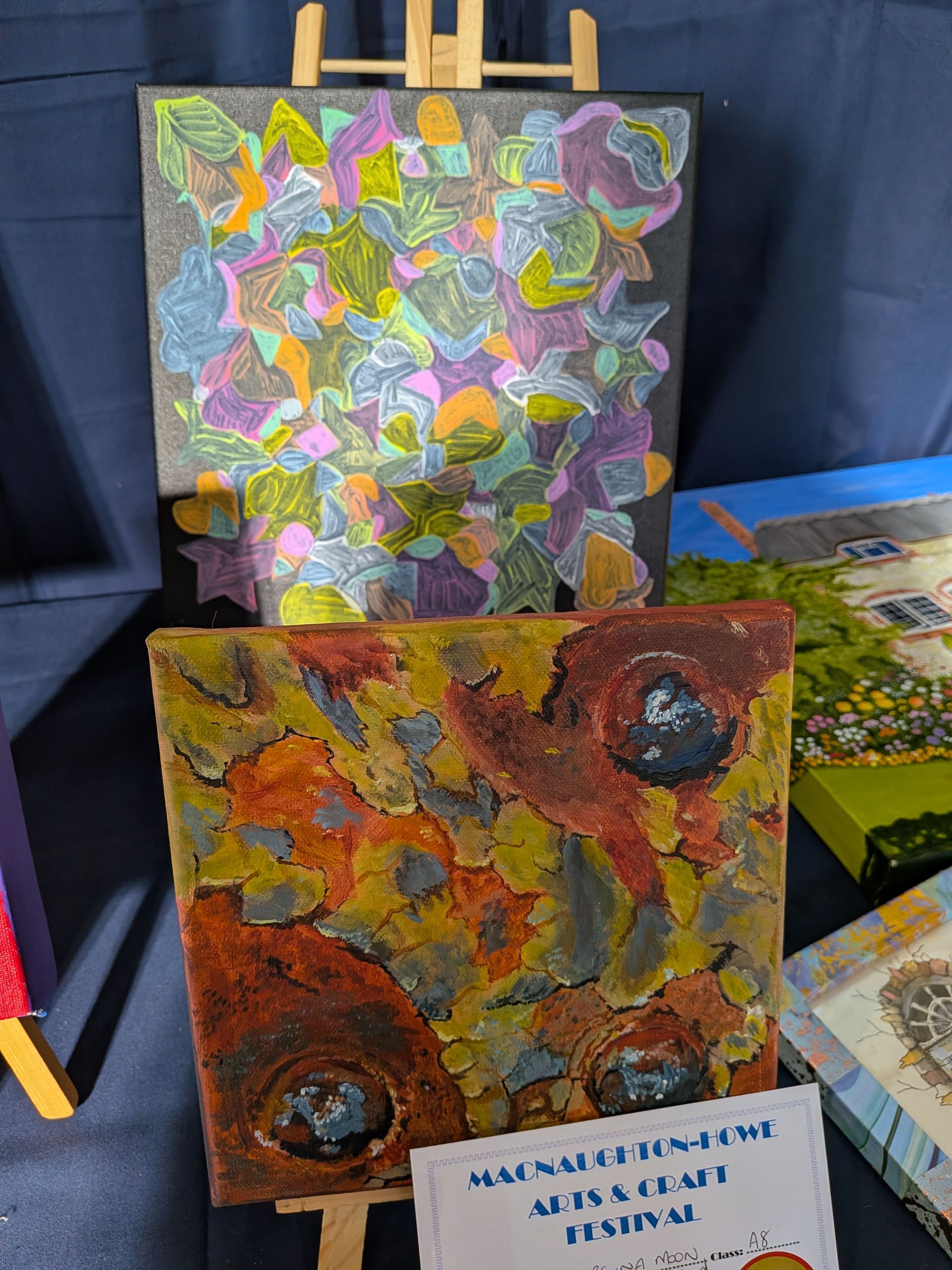 Paintings on easels: abstract colorful leaves, textured rust and ochre, and a landscape.