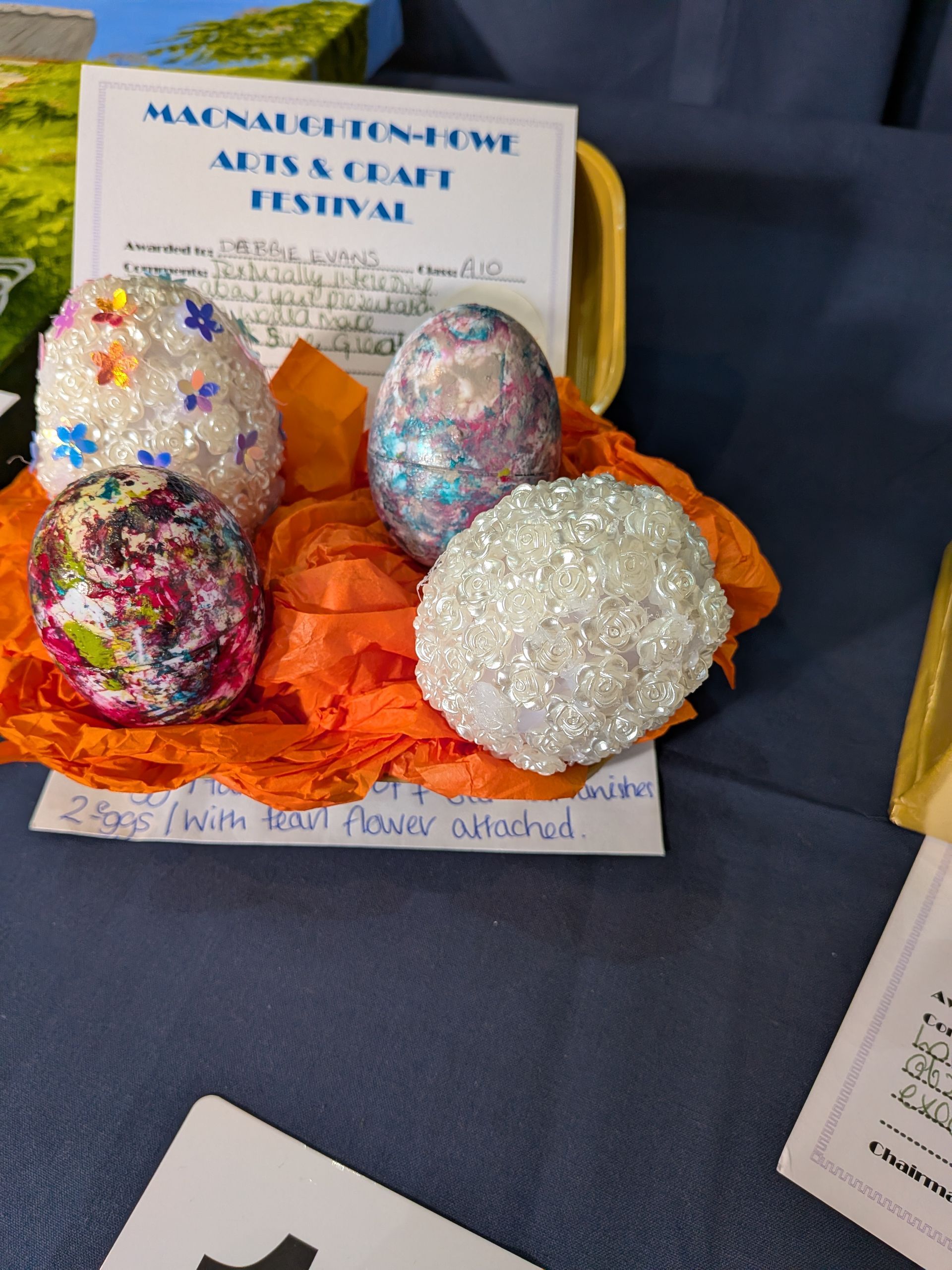Glitter-covered decorative eggs on orange tissue paper at an art festival.