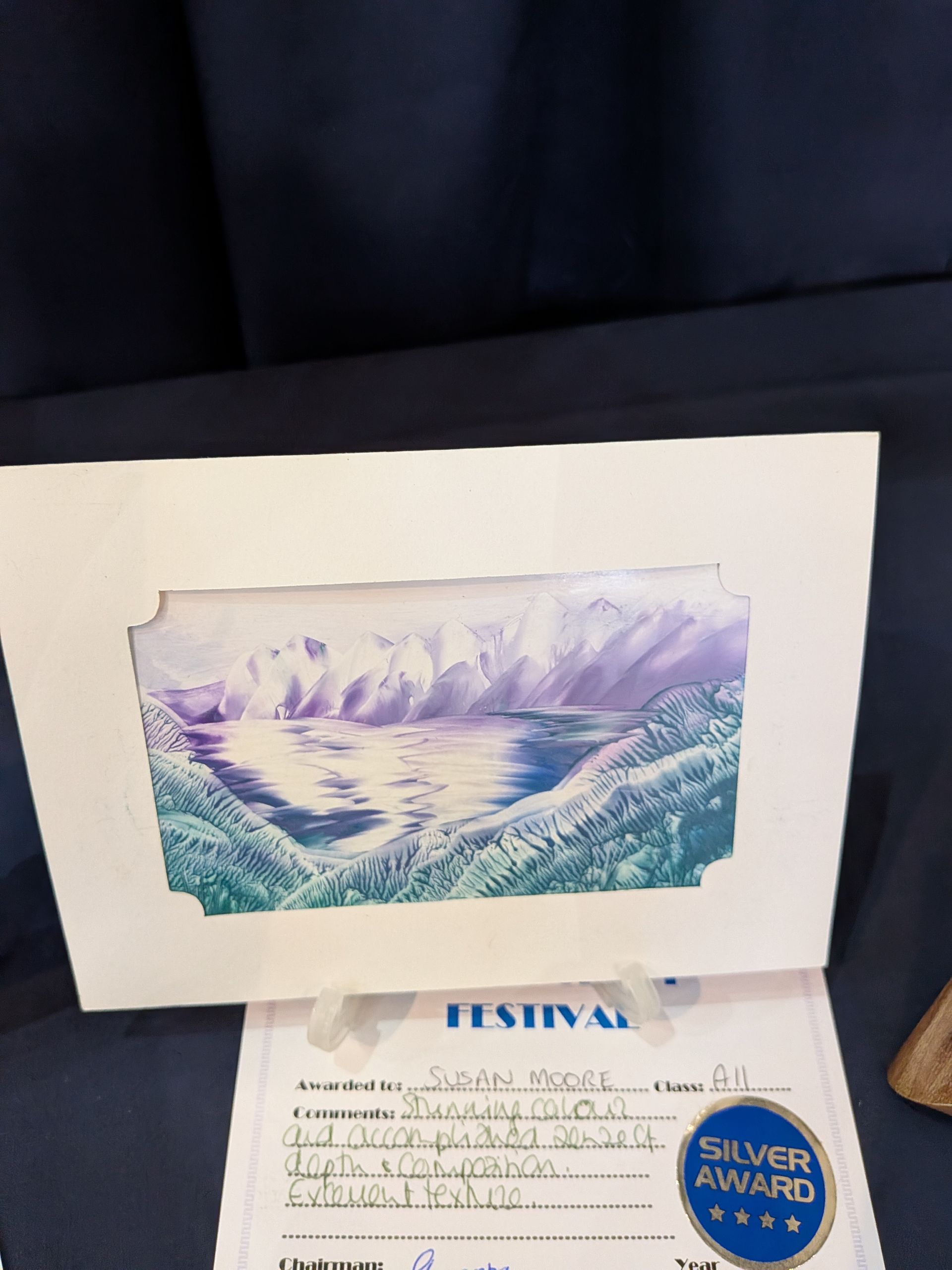 Watercolor landscape of mountains and water, framed, with a silver award certificate.