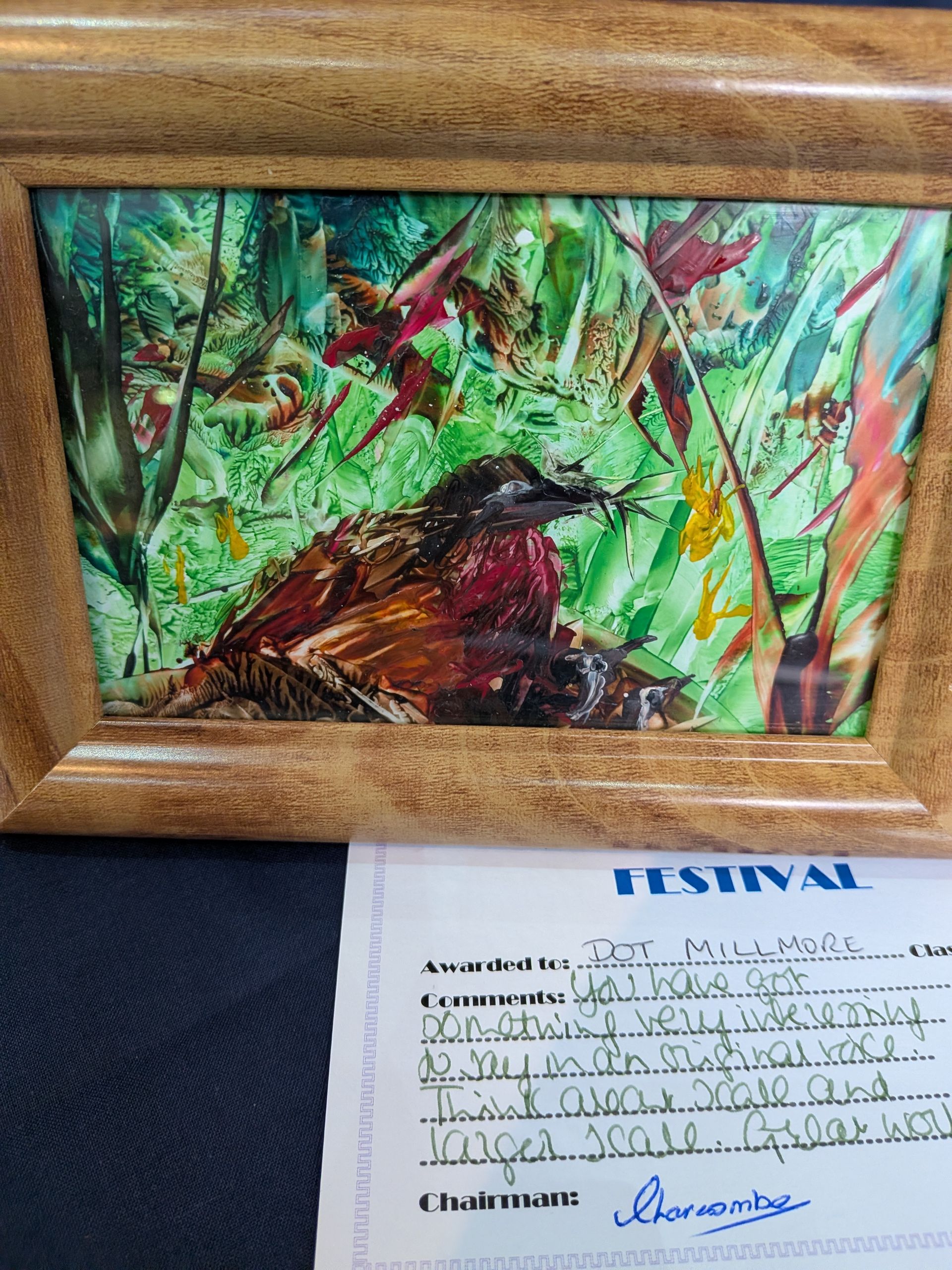 Painting of a bird in a lush, green environment, with a frame and a handwritten festival award document below.