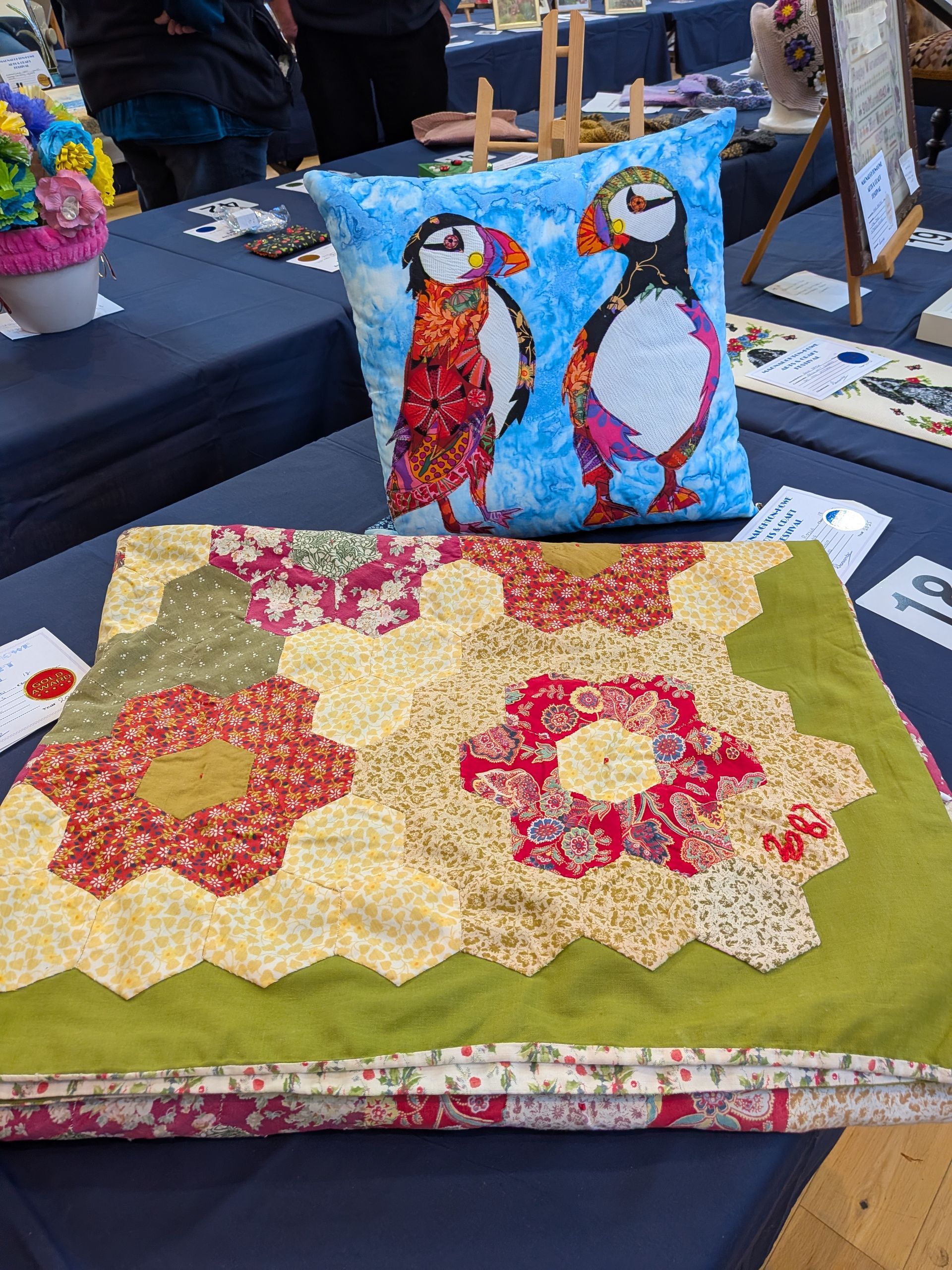 Puffin pillow and floral quilt on a blue tablecloth. Red, yellow, and green fabrics.