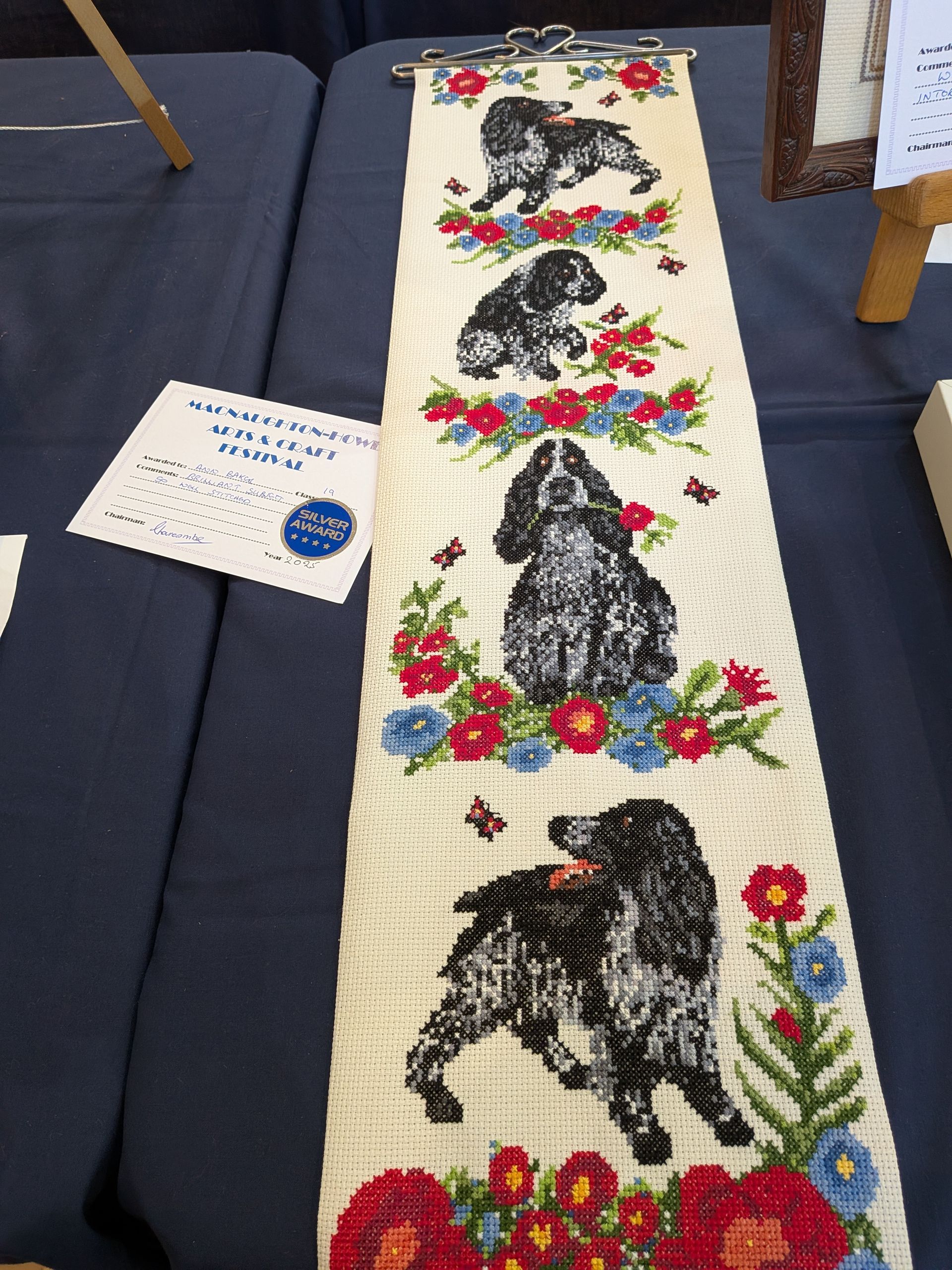 Cross-stitch of four black and white spaniels with floral borders on a cream background.