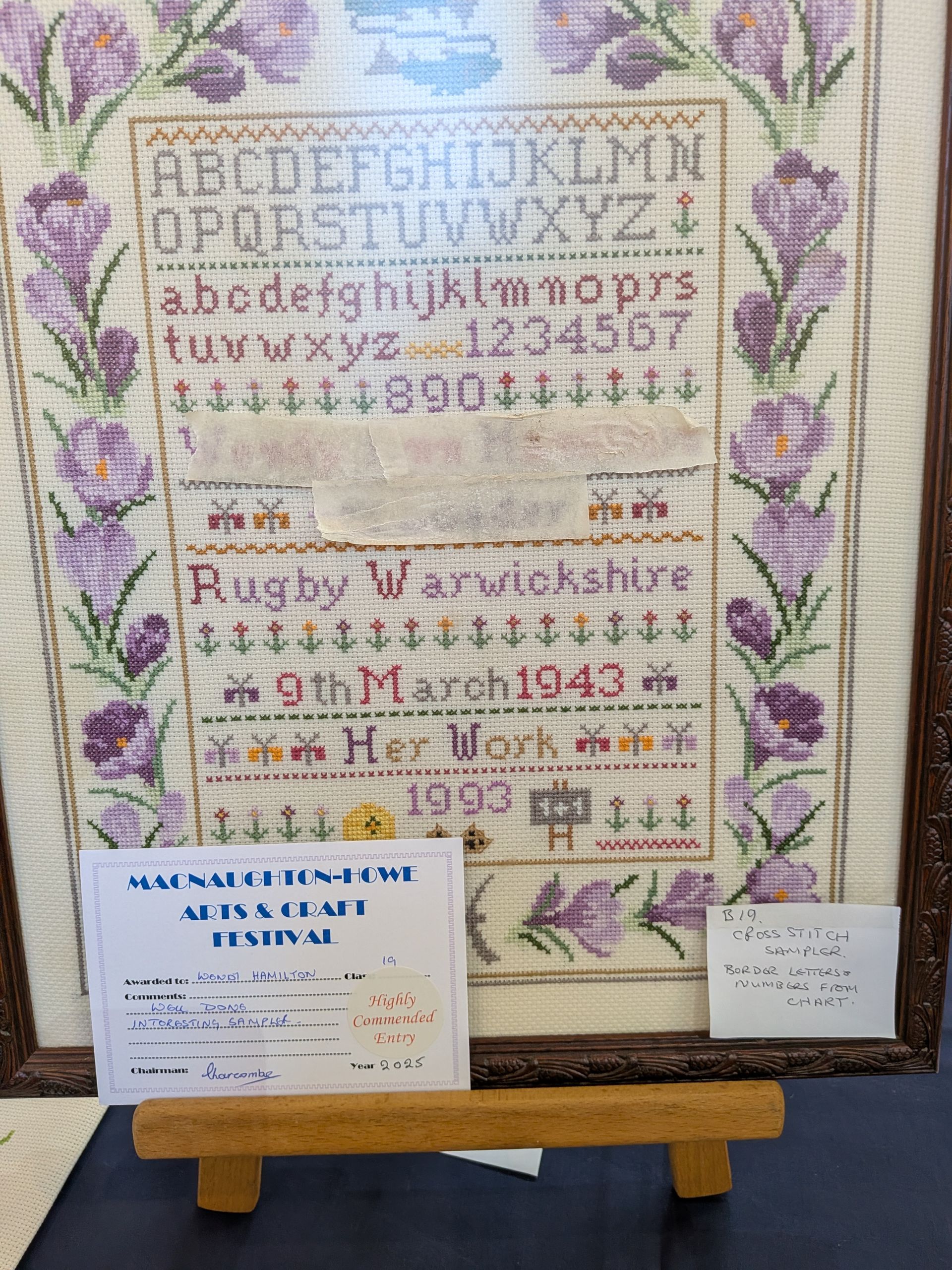 Cross-stitch sampler with floral border, lettering, and text including 