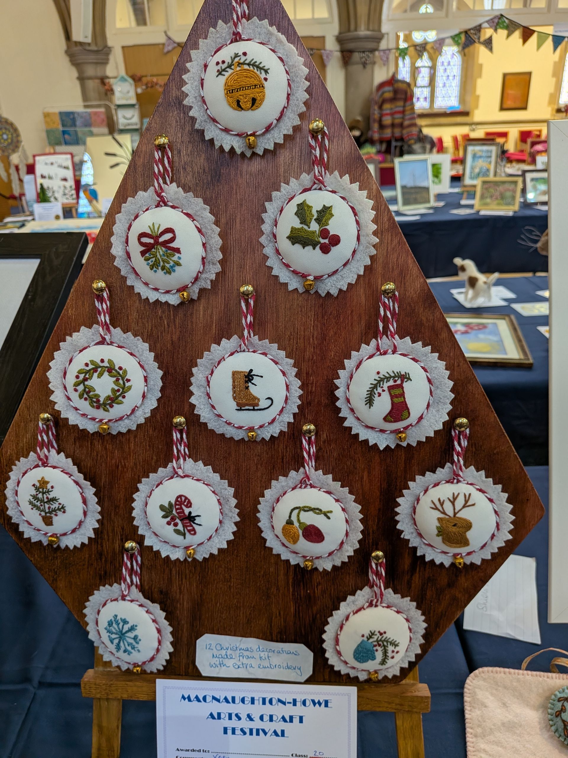 A wooden display with cross-stitched Christmas ornaments in a church setting.