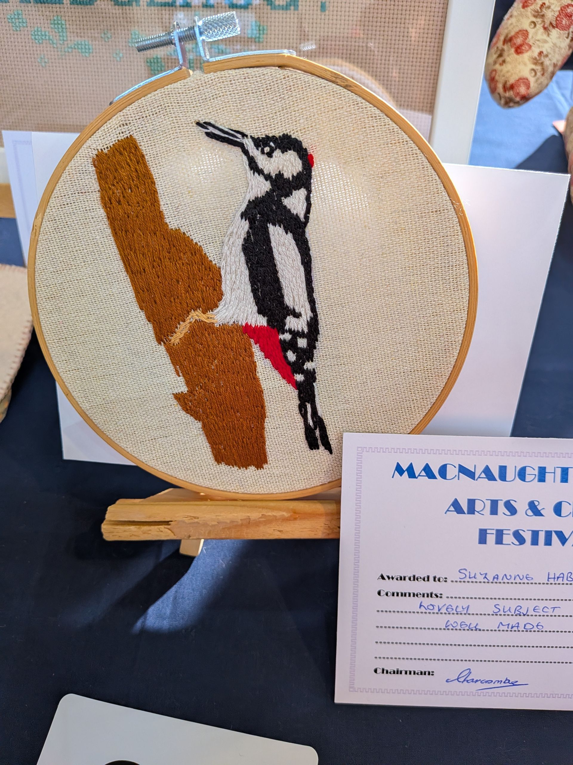 Embroidery hoop art of a woodpecker on a branch; displayed with festival certificate.