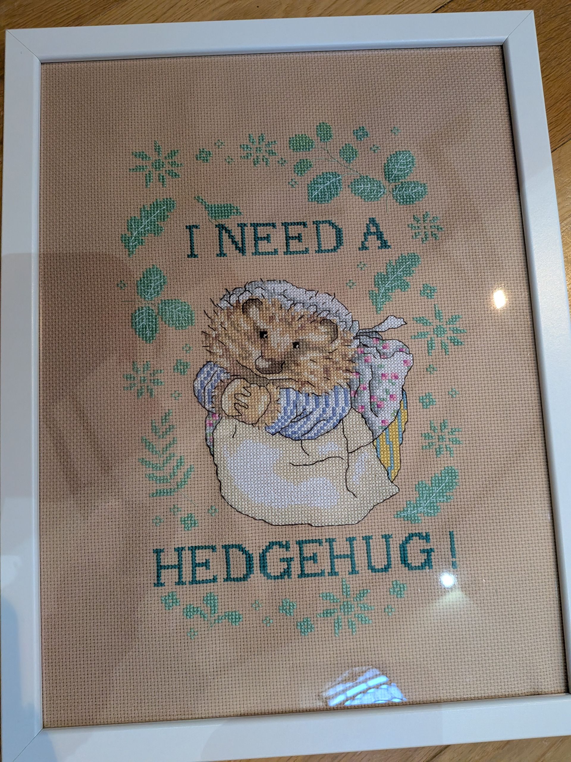 Cross-stitch of a hedgehog in a cup, with text 