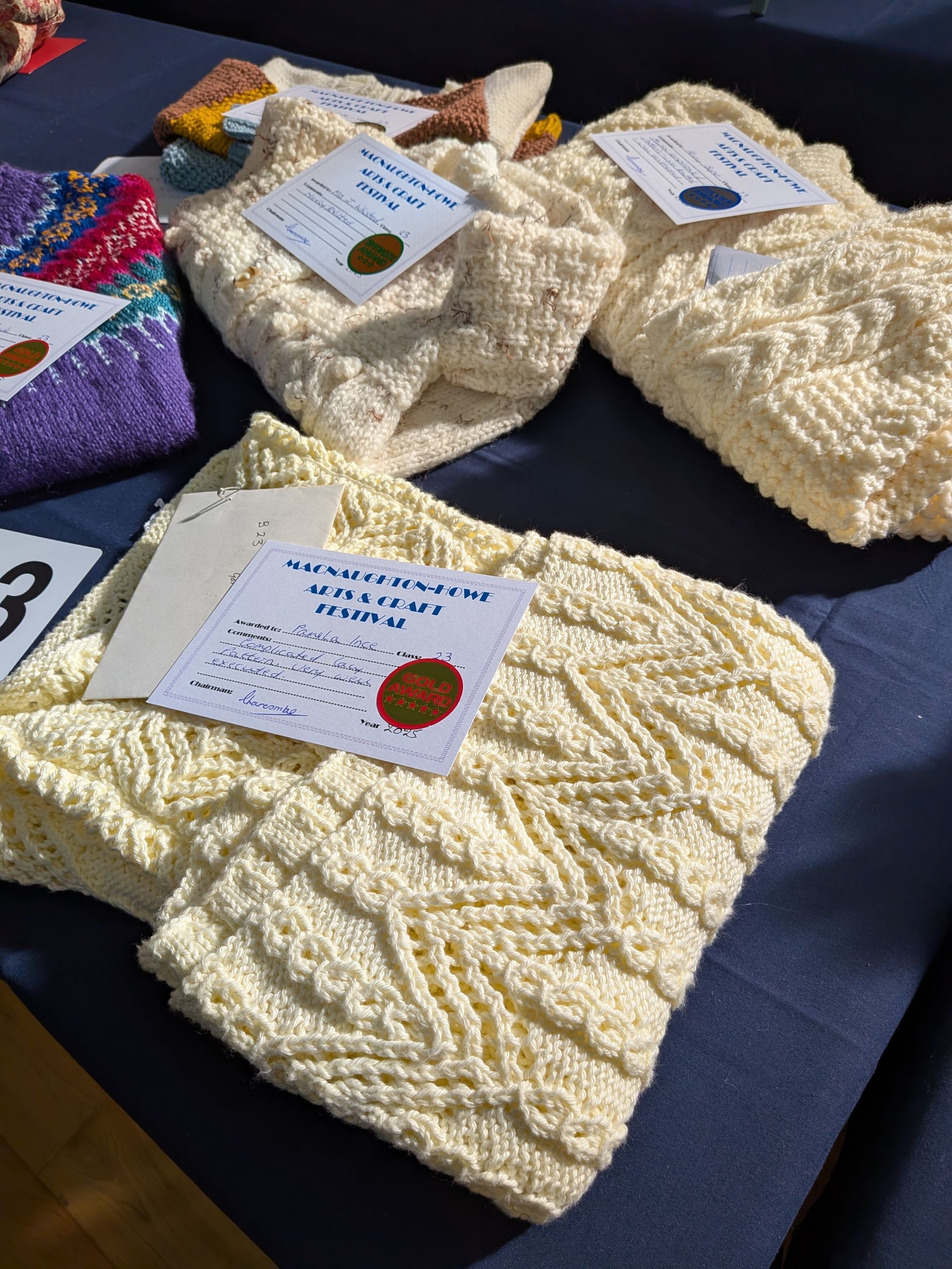 Close-up of knitted cream-colored items, likely handcrafts, on a blue surface, each with a tag.