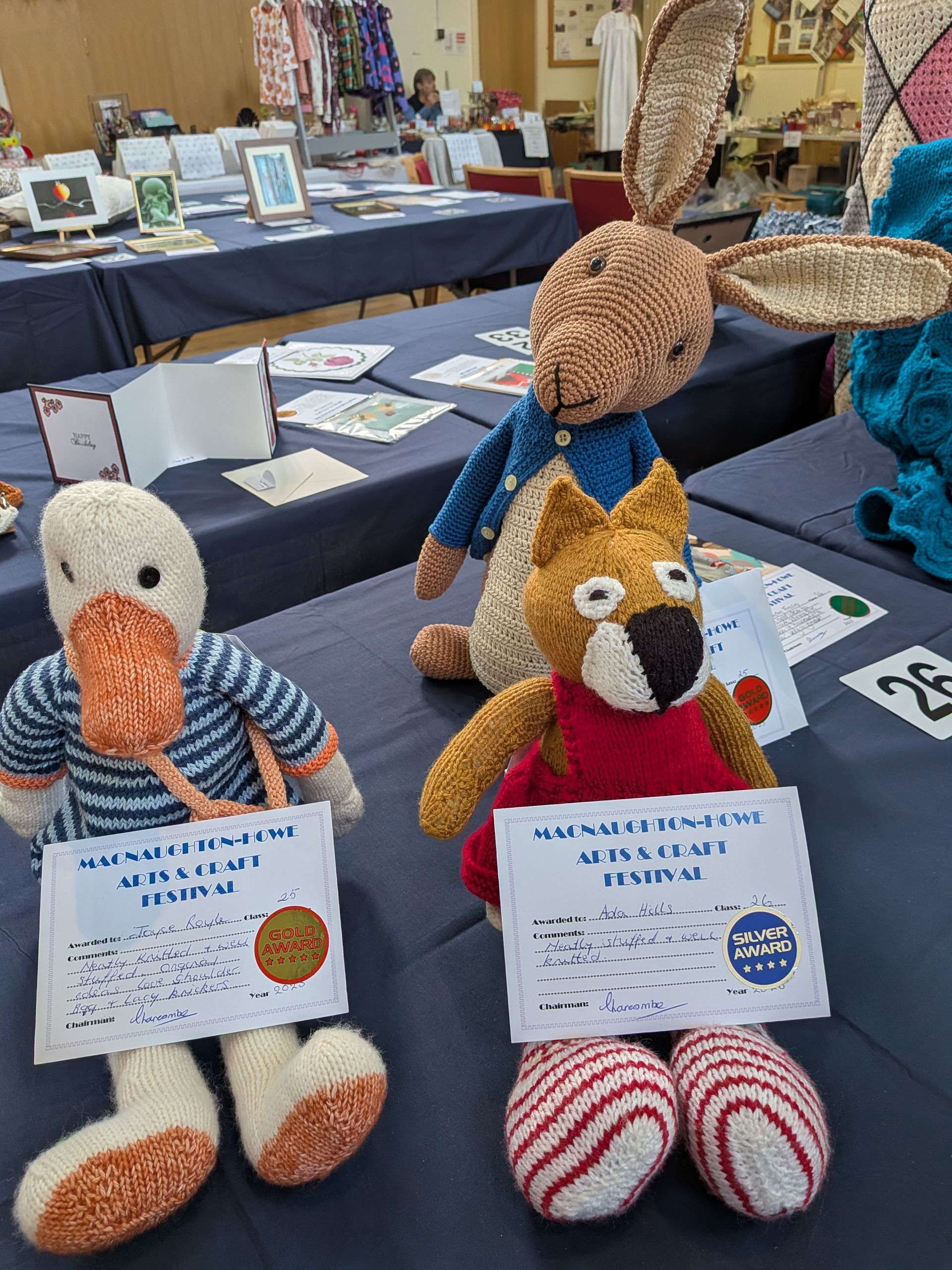 Knitted duck, fox, and bunny toys with festival signs displayed on a table.