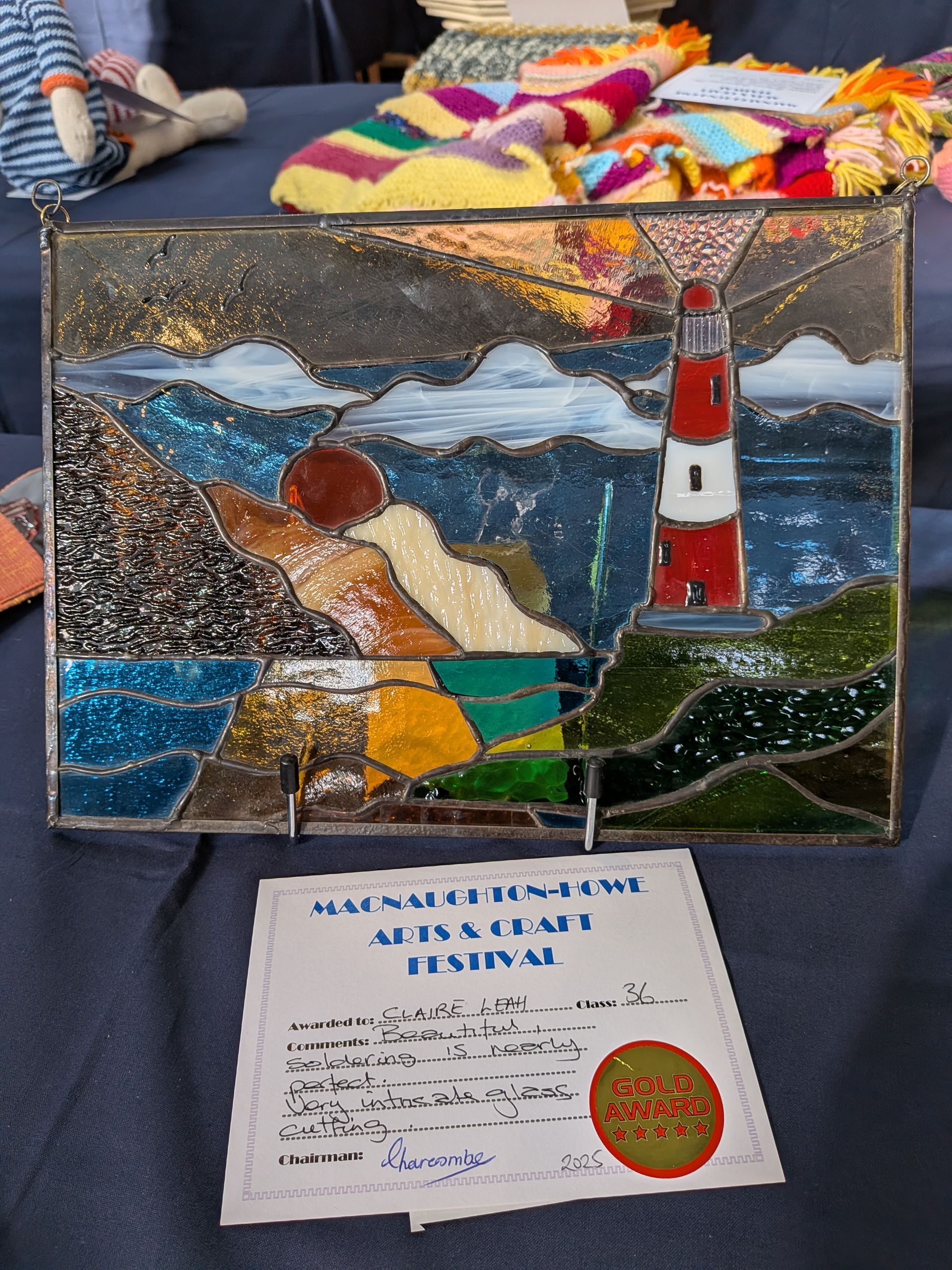 Stained glass panel depicting a lighthouse on a rocky coast with blue water and sky.