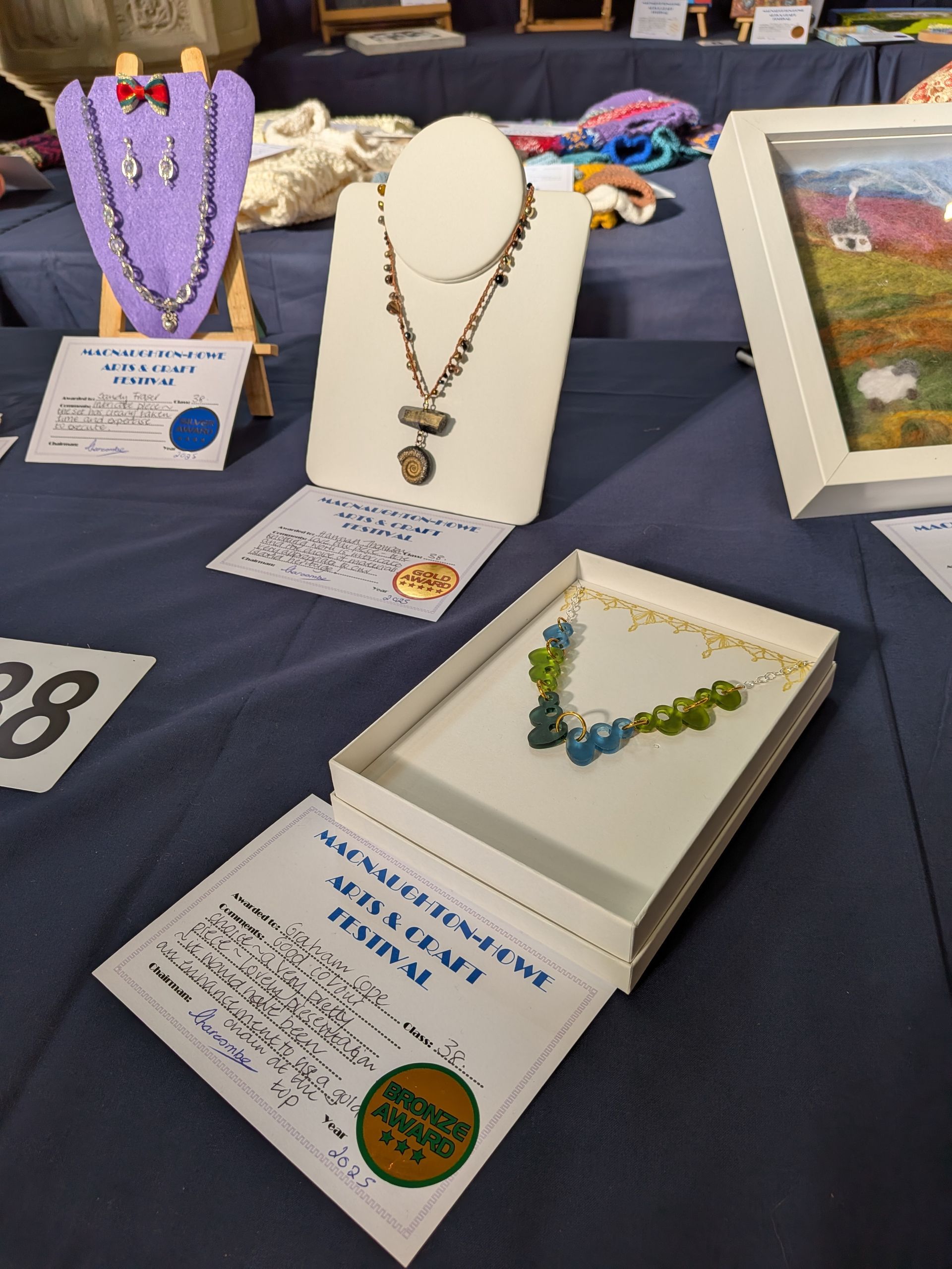 Jewelry display on blue tablecloth: necklaces, earrings, and artwork.