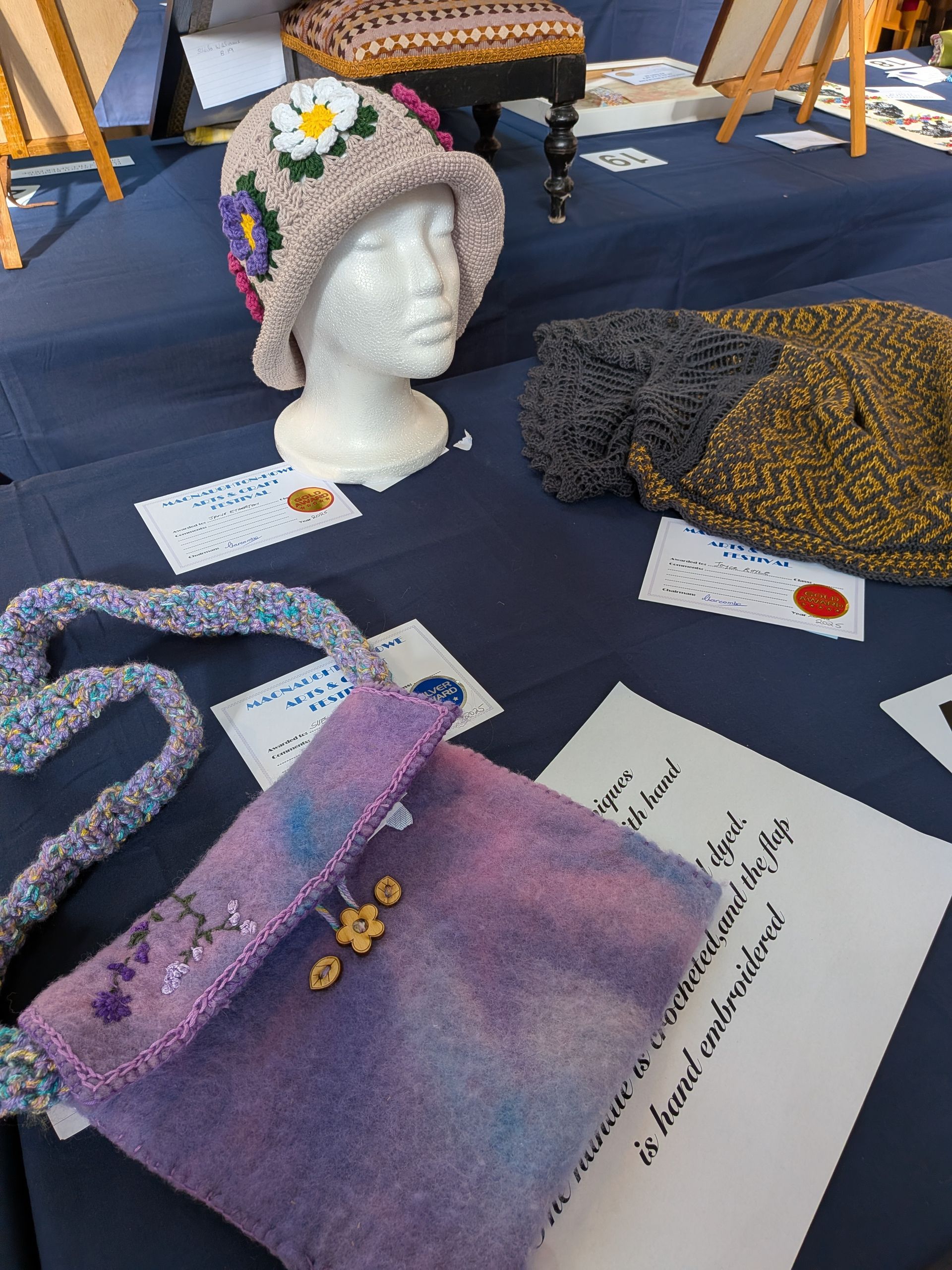 Handmade crafts on a blue table: a hat with daisy, felt purse, and other textiles, displayed with cards.