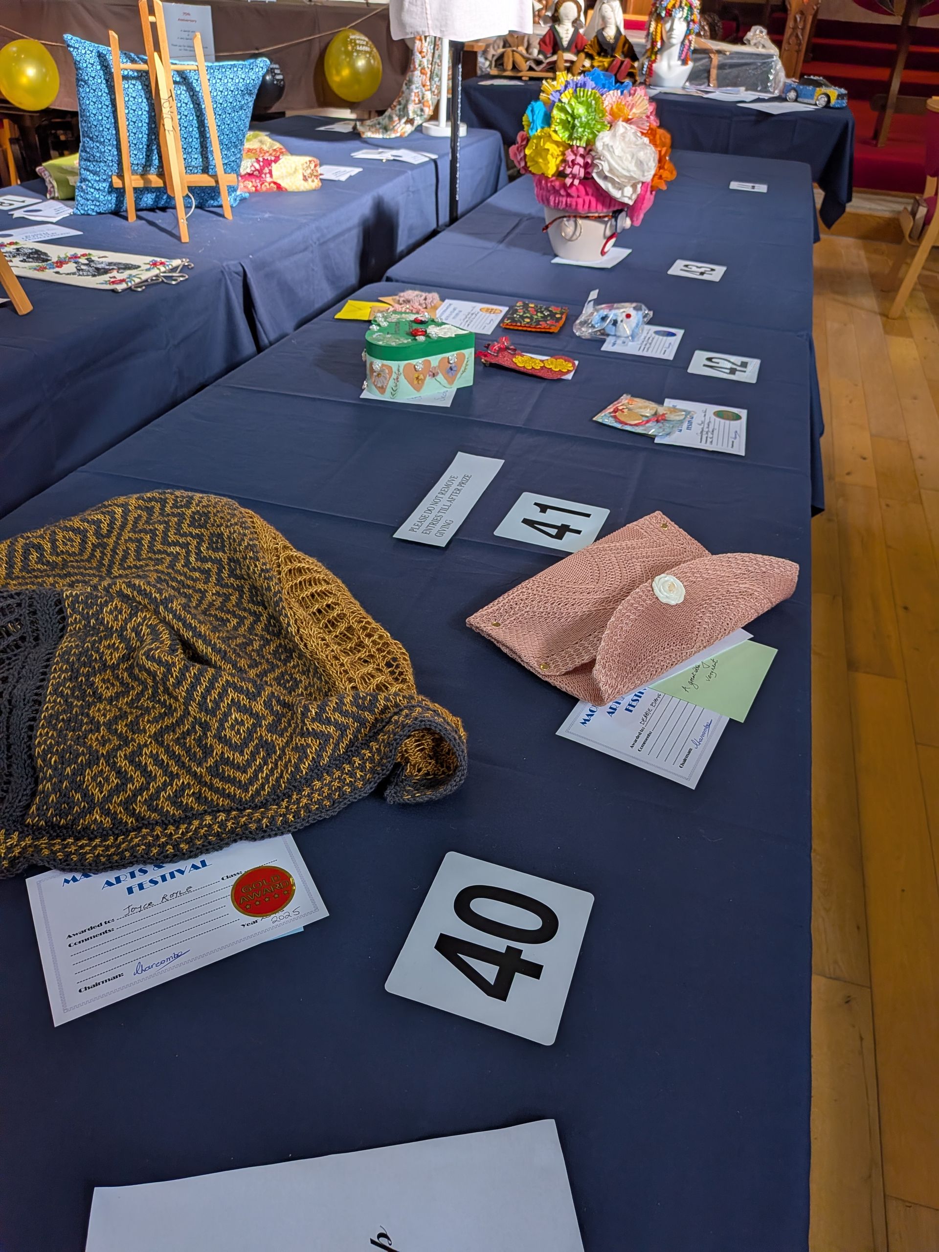 Long table displays: knitted items, craft flowers, and numbered auction cards.