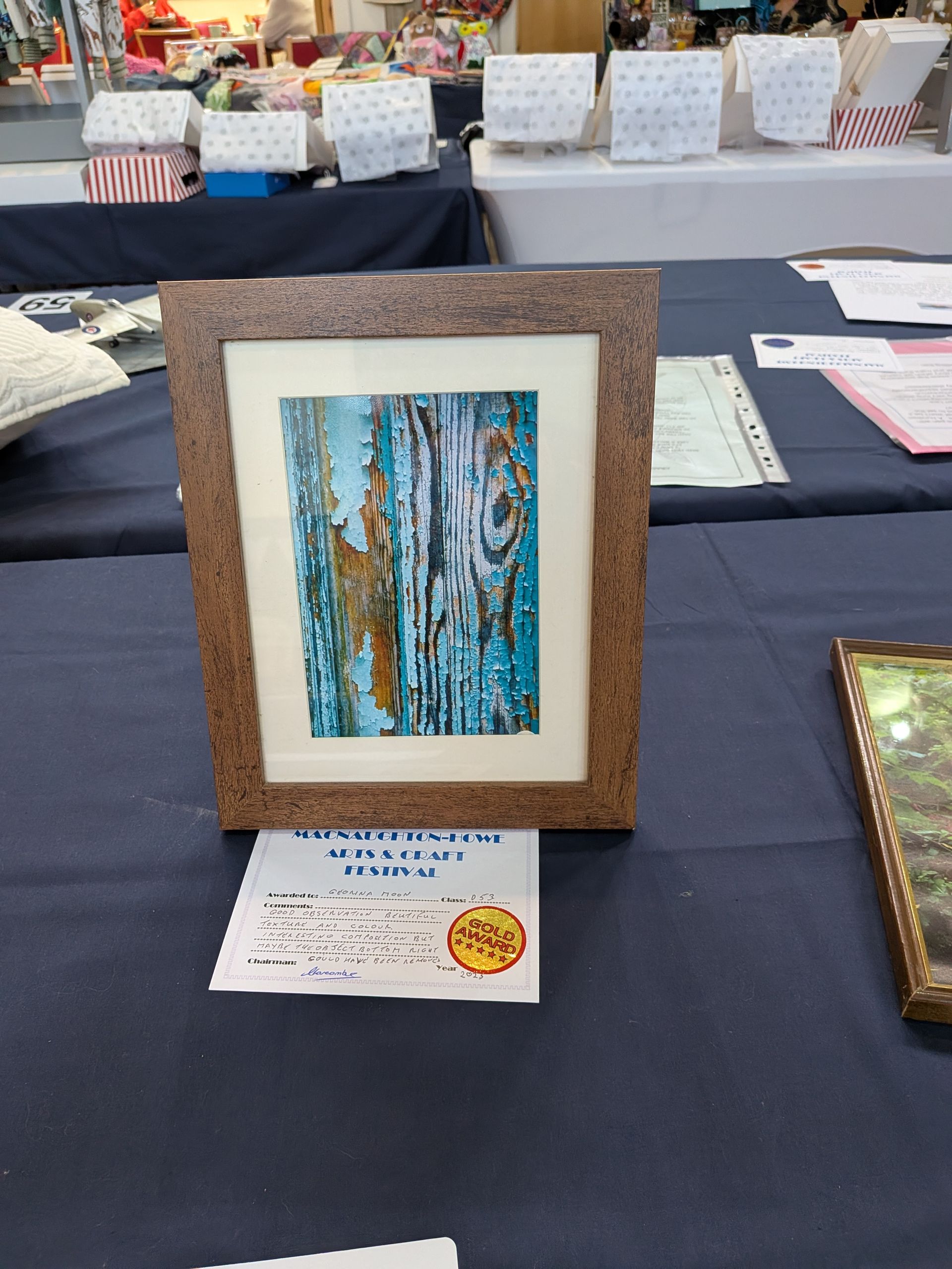 Framed artwork of blue and brown abstract figures, on a display table with a white label.