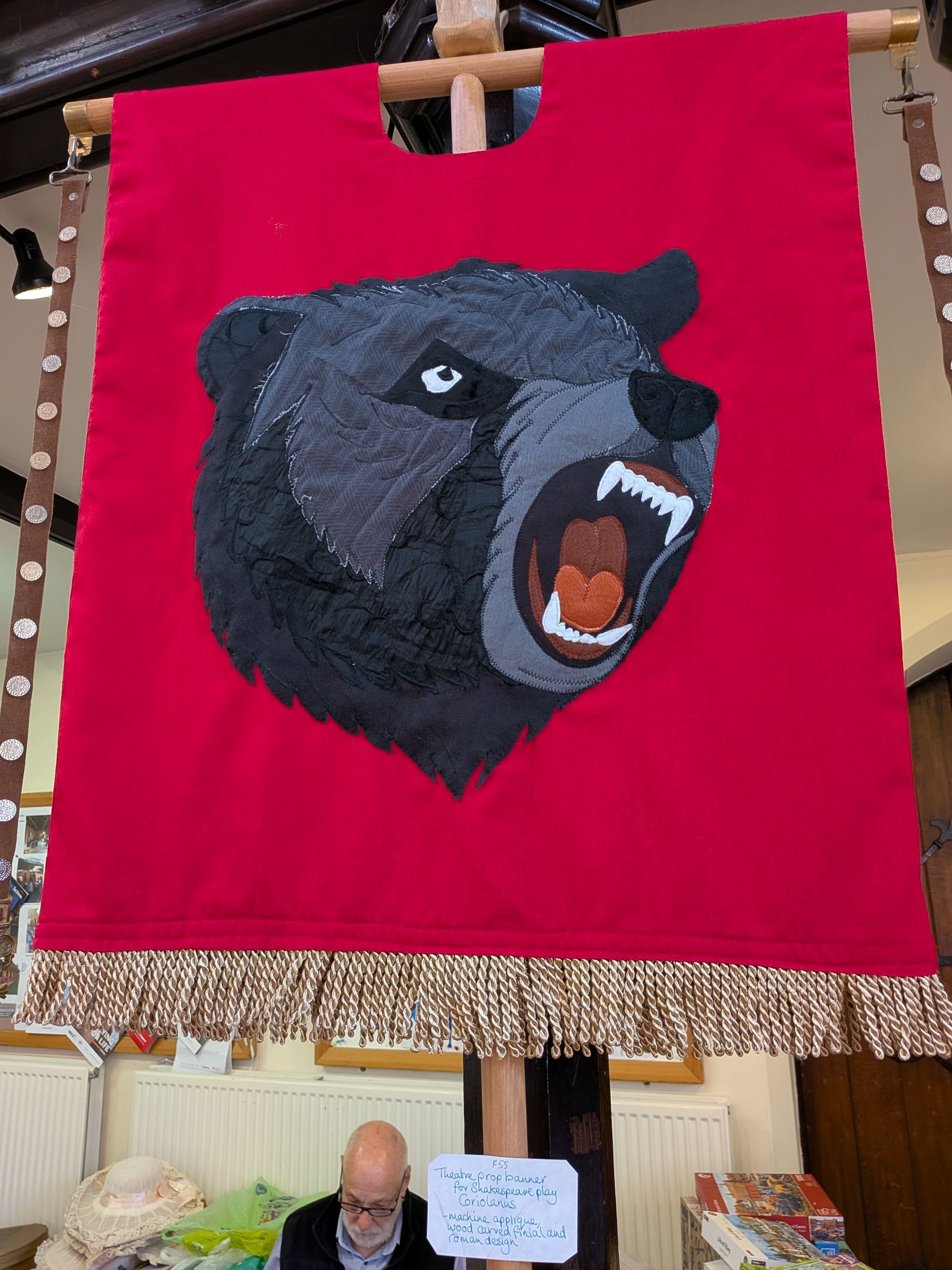 Red banner with embroidered bear head. Beige fringe along the bottom.