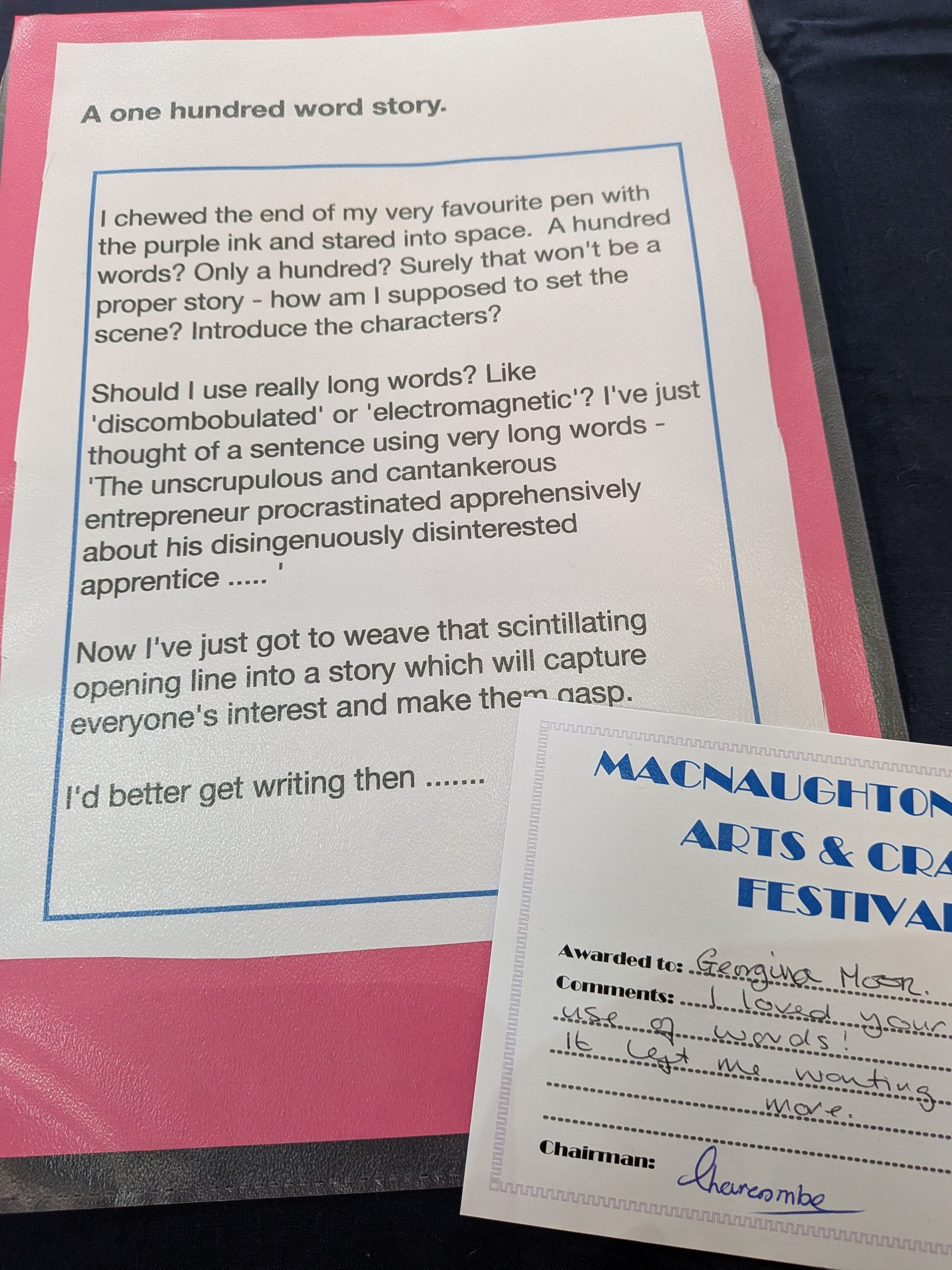 A pink-framed paper with a handwritten story, next to a festival card. Both sit on a dark surface.