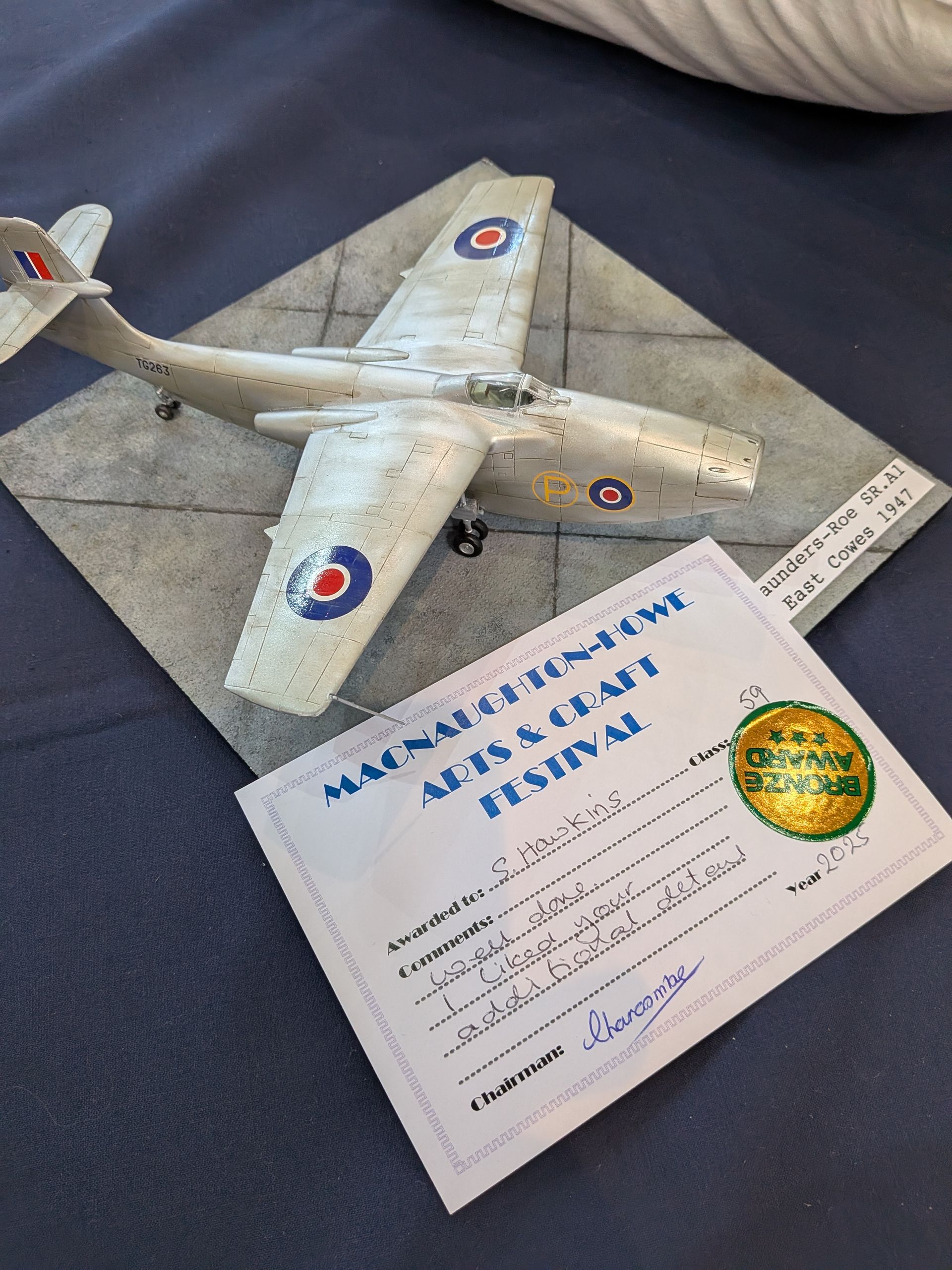 Model airplane with British markings and an award certificate on a blue surface.