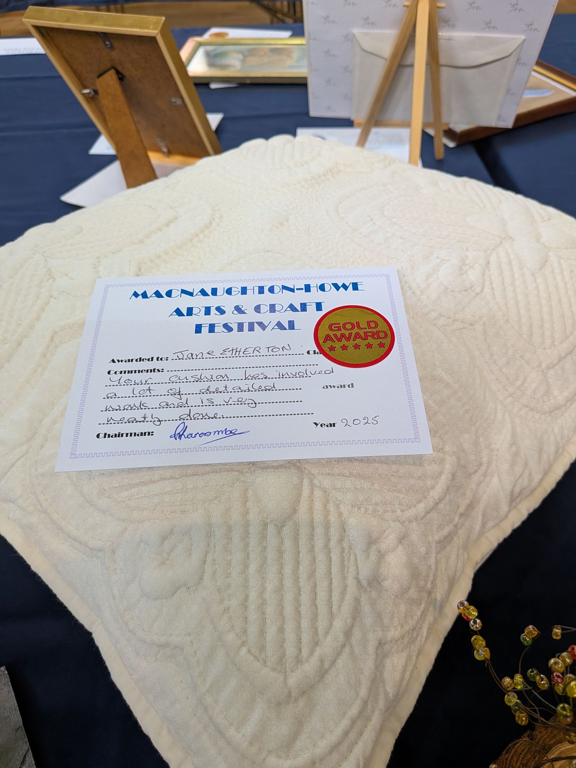 Cream-colored knitted blanket with an award certificate on display at an art festival.