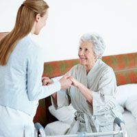 Elderly woman receiving help from a woman out of bed