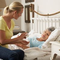 elderly woman in bed while adult woman sits at her bedside