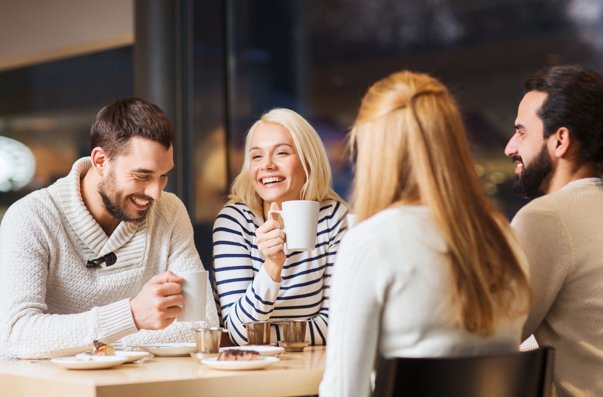 Four friends laughing around a table in a cafe, enjoying coffee and conversation.