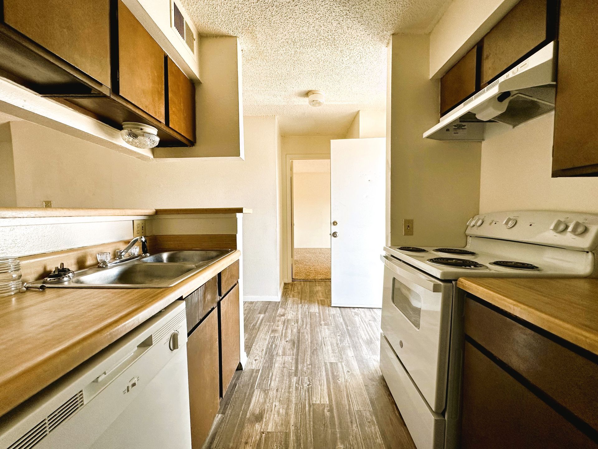 Kitchen with wooden cabinets, white appliances, and a hallway leading to a door.