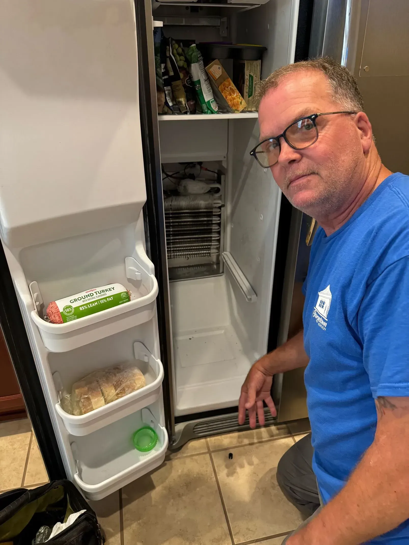 A man in a blue shirt is standing in front of an open refrigerator.