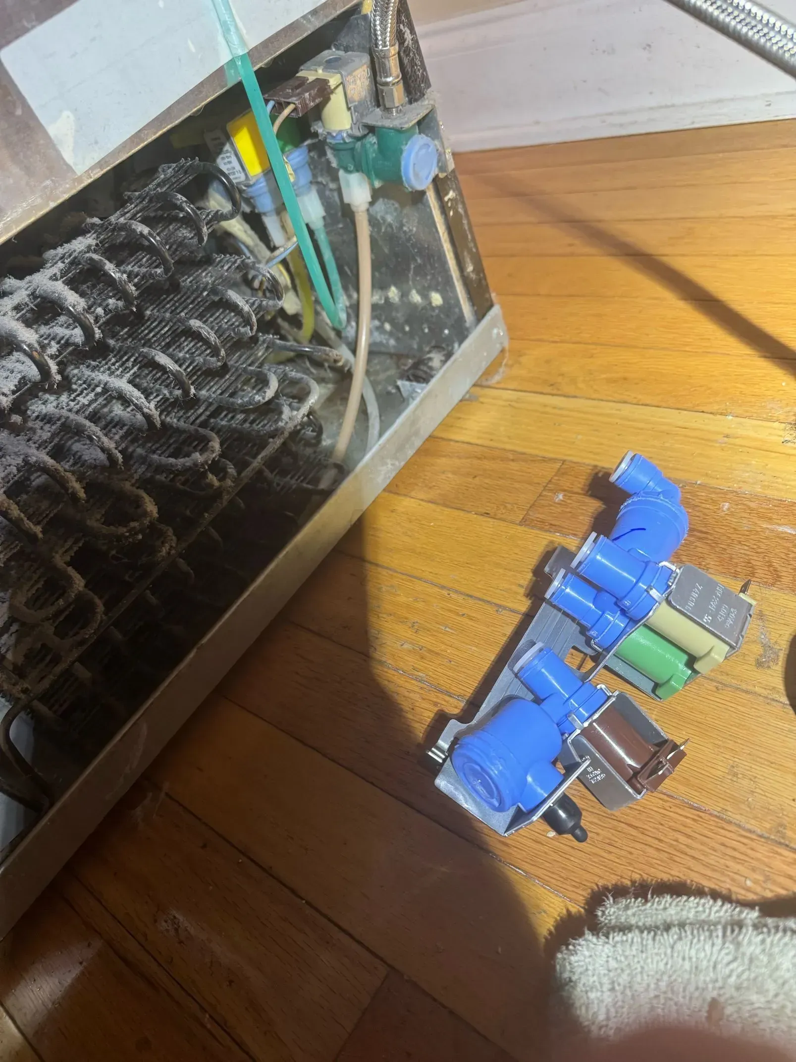 A person is standing next to a broken refrigerator on a wooden floor.