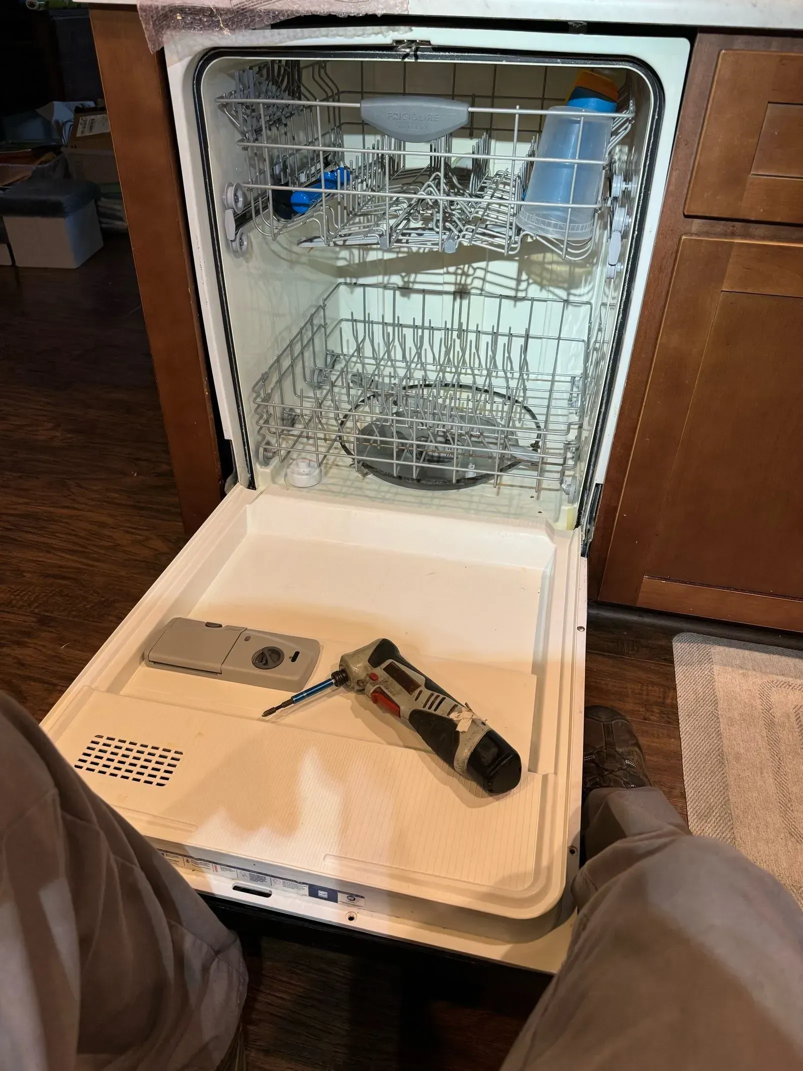 A person is sitting in front of a dishwasher with the door open.