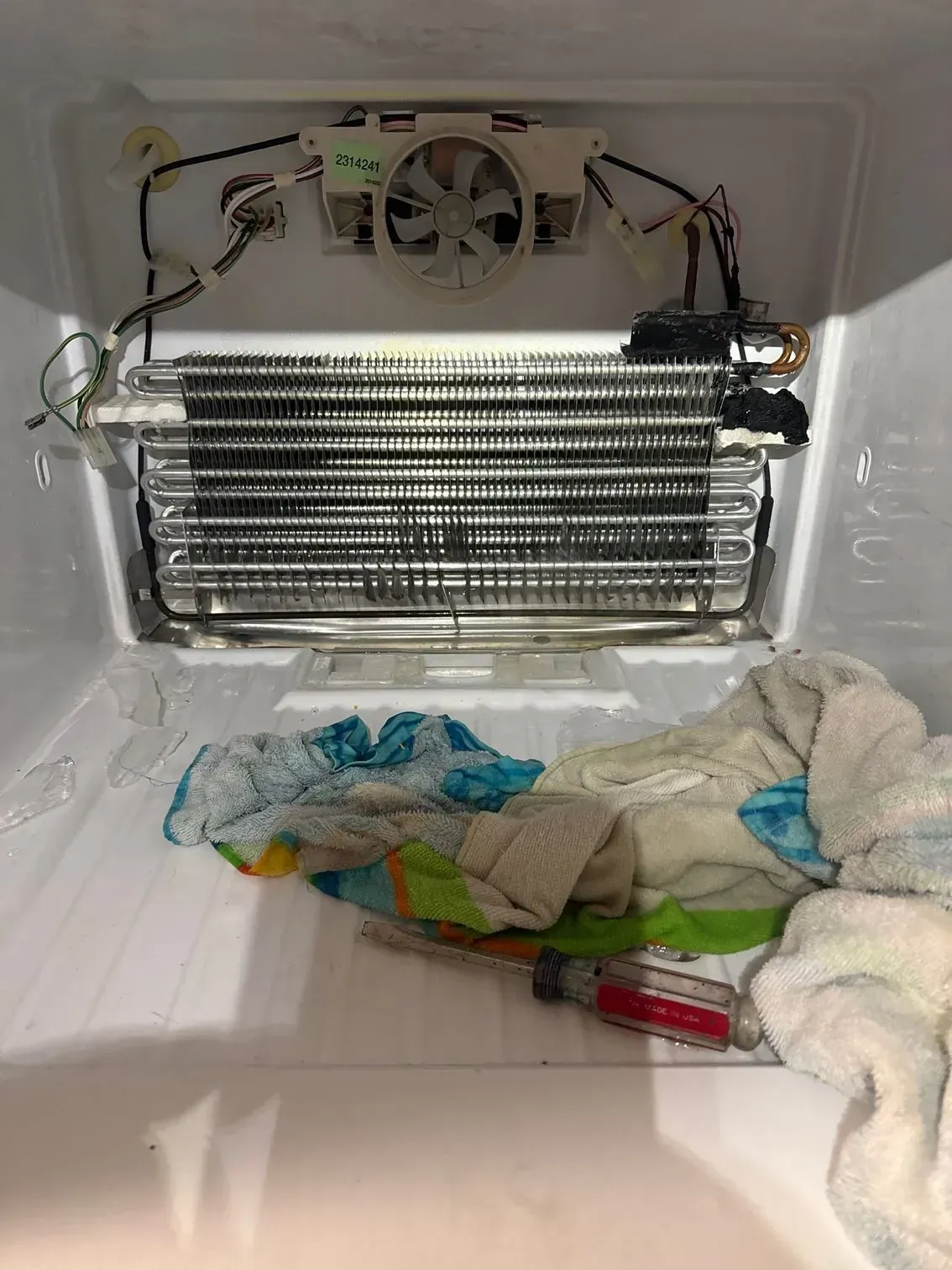 The inside of a refrigerator with a towel and a screwdriver on the floor.