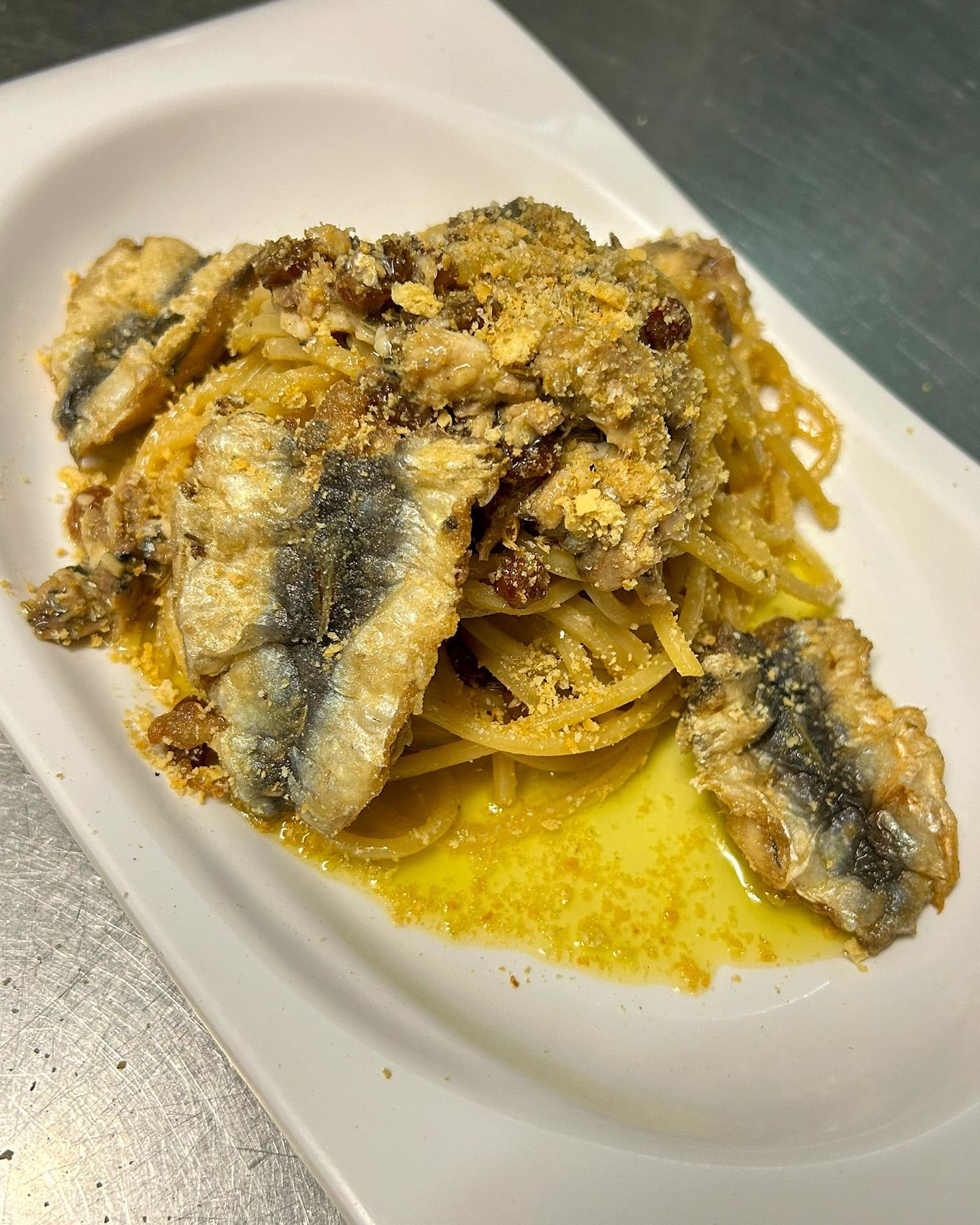 Piatto di spaghetti con pesce fritto e pangrattato, servito su un piatto bianco rettangolare.