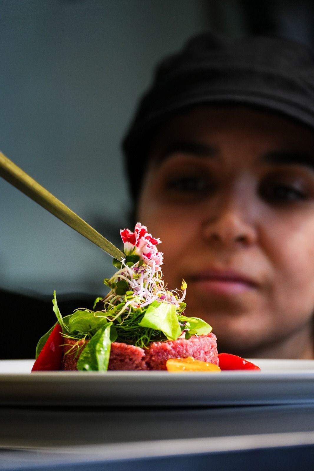 Uno chef guarnisce un piatto con verdure fresche, in una cucina professionale.