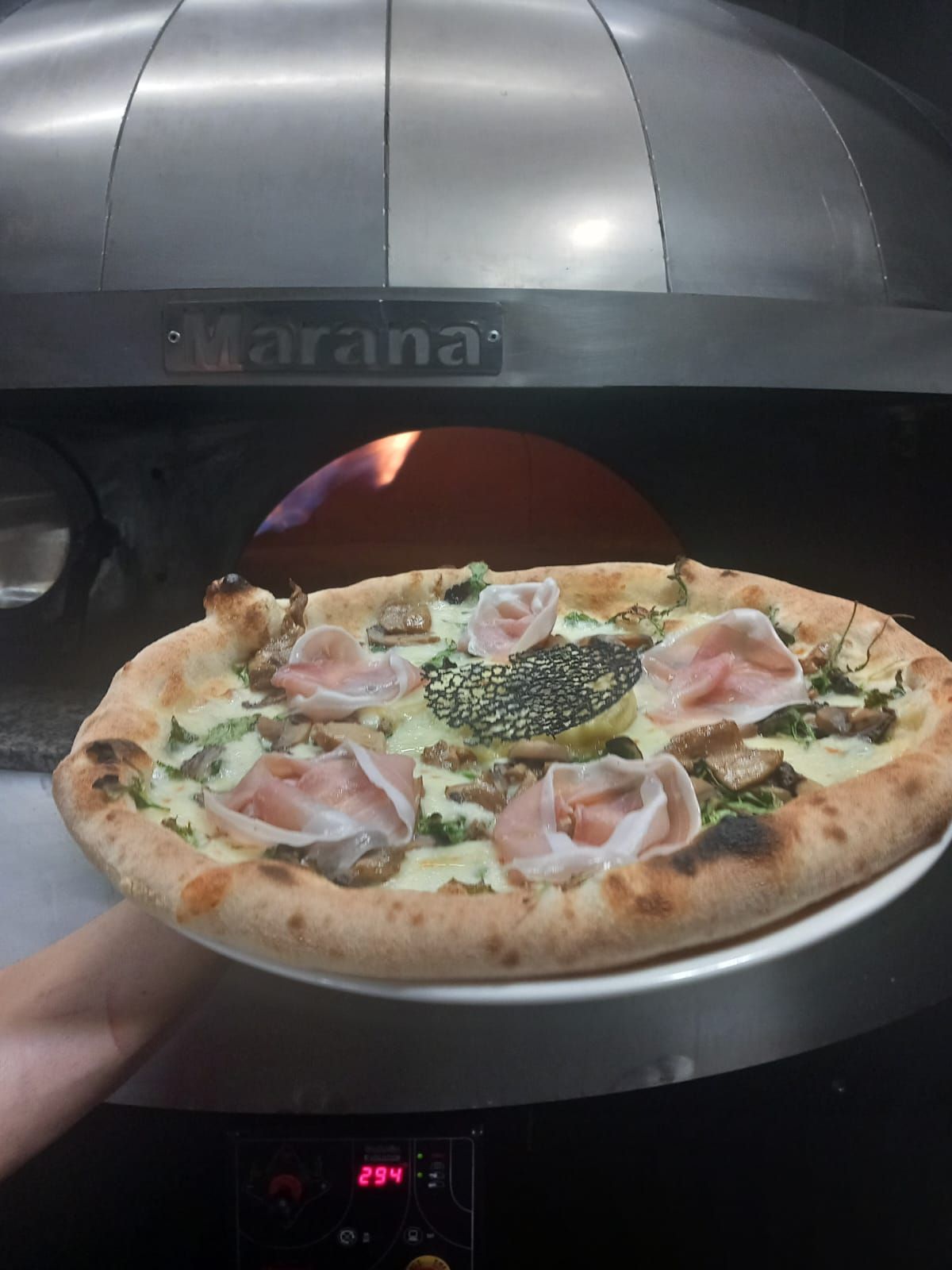 Pizza con prosciutto servita davanti al forno per pizza.